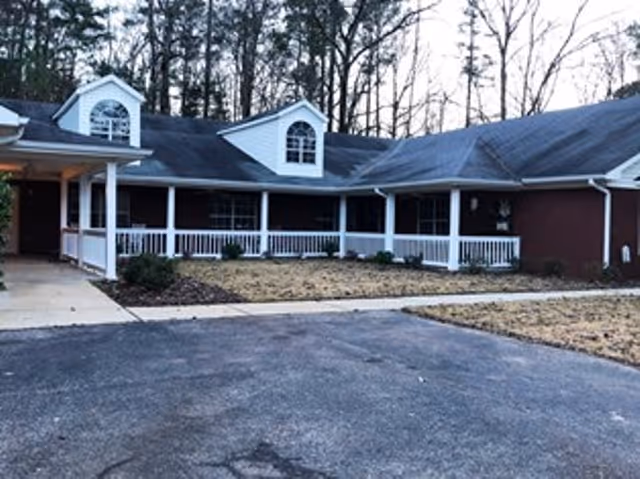 Single-story brick senior living building with a white wraparound porch and dormer windows.