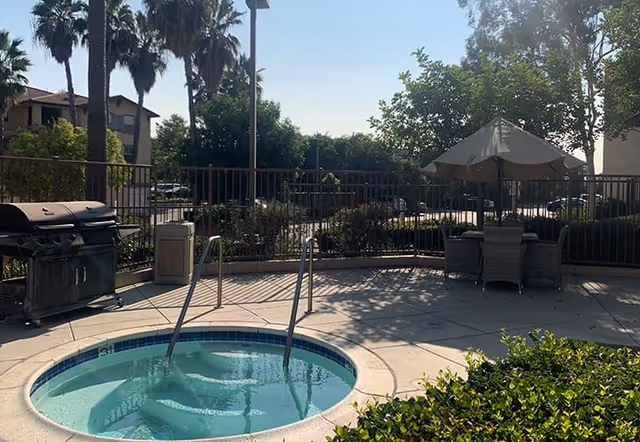 Outdoor pool and patio area with chairs, umbrella, grill, and railing.