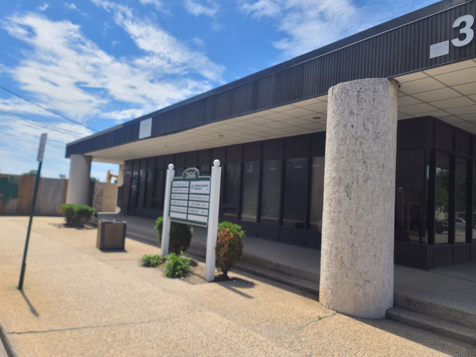 Exterior view of a modern building with glass storefront, large concrete columns, under blue sky.