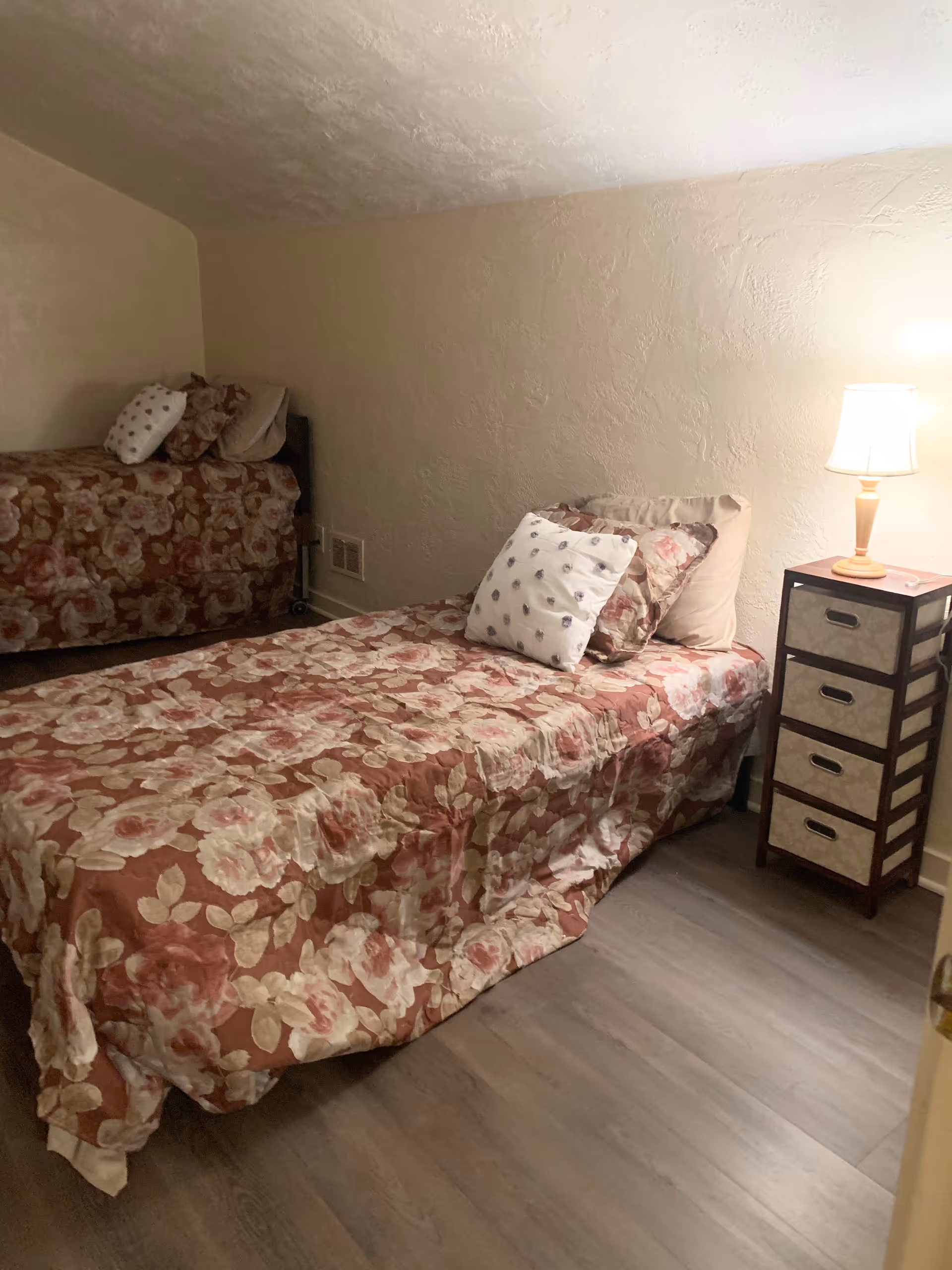 Two twin beds with floral bedding in a small, warmly lit bedroom.