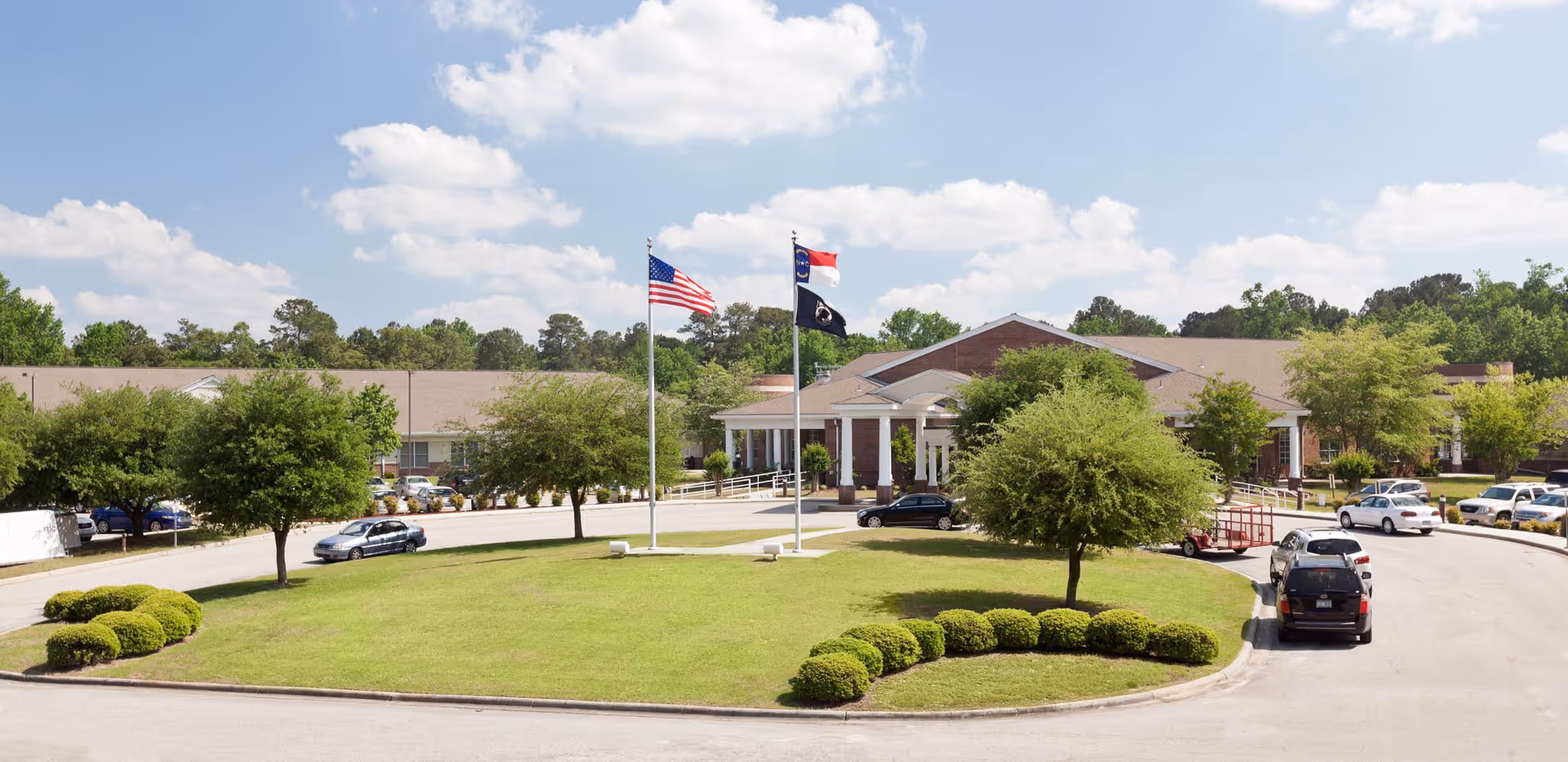 Exterior view of NC State Veterans Home Fayetteville with flagpoles and driveway.