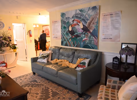 Cozy senior living lobby with teal sofa, tropical wall art, and a person visible in background.