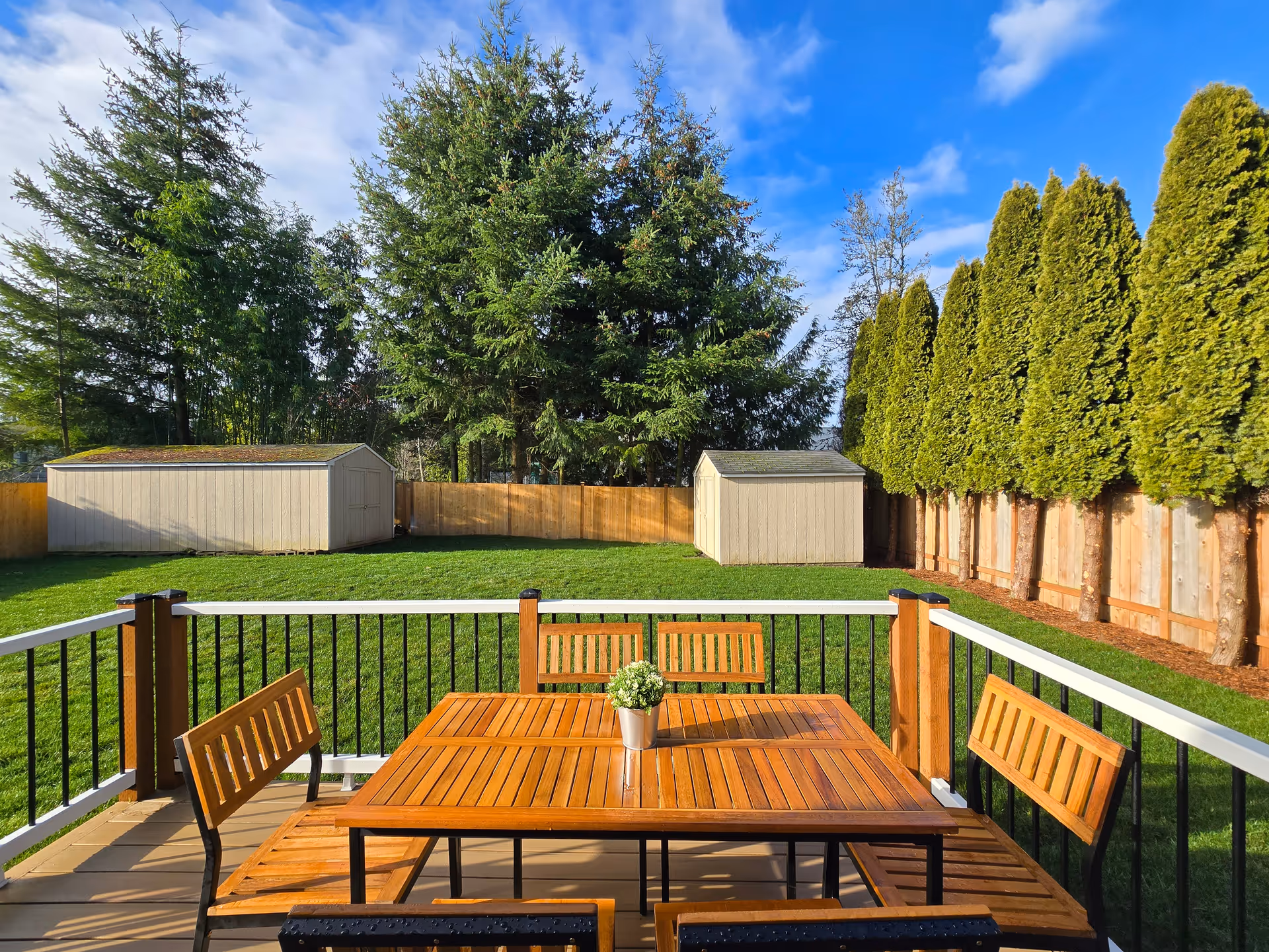 Patio table and chairs on a deck overlooking a grassy yard and sheds.