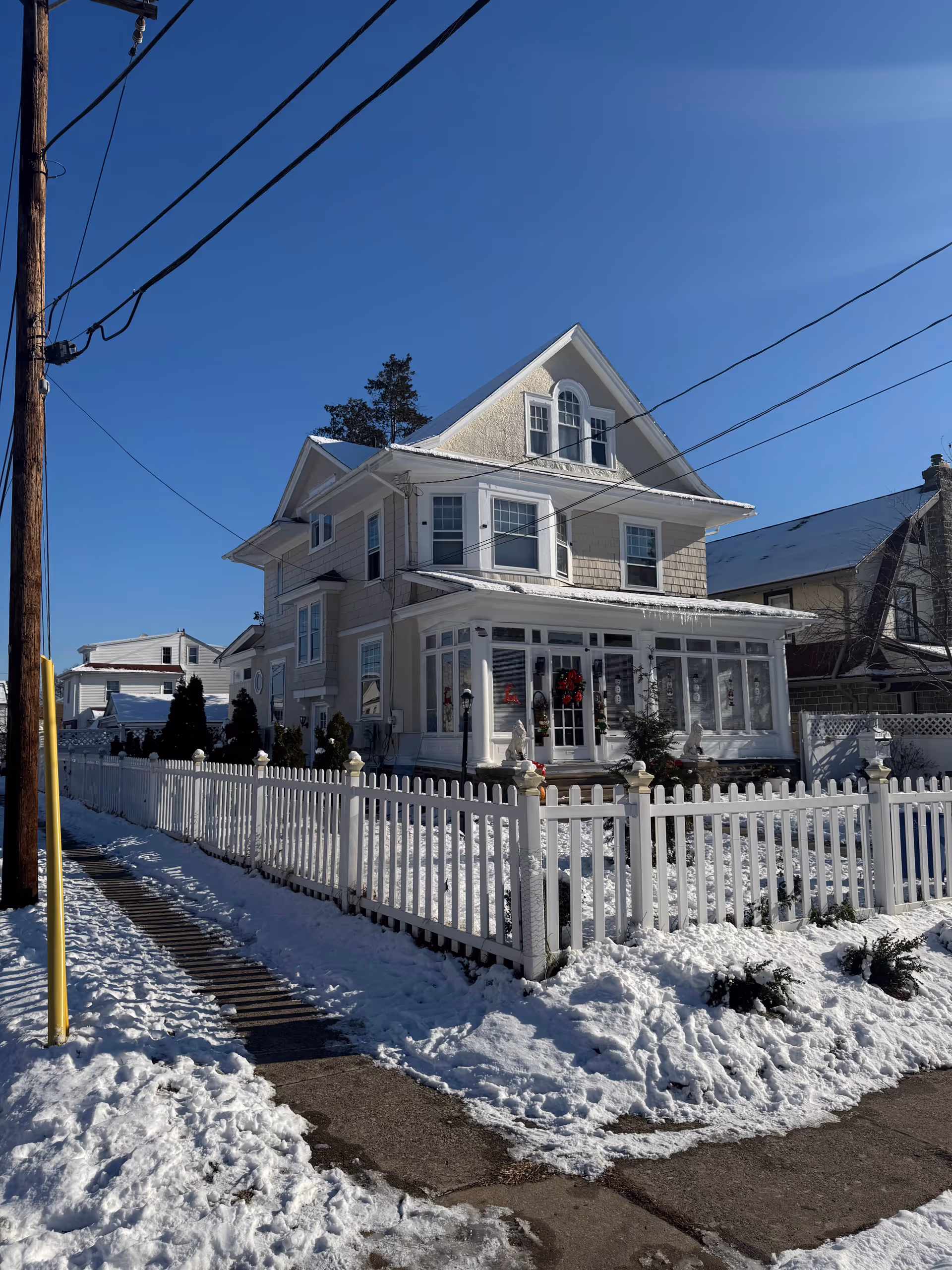 Two-story beige house with a white picket fence and snow-covered yard.