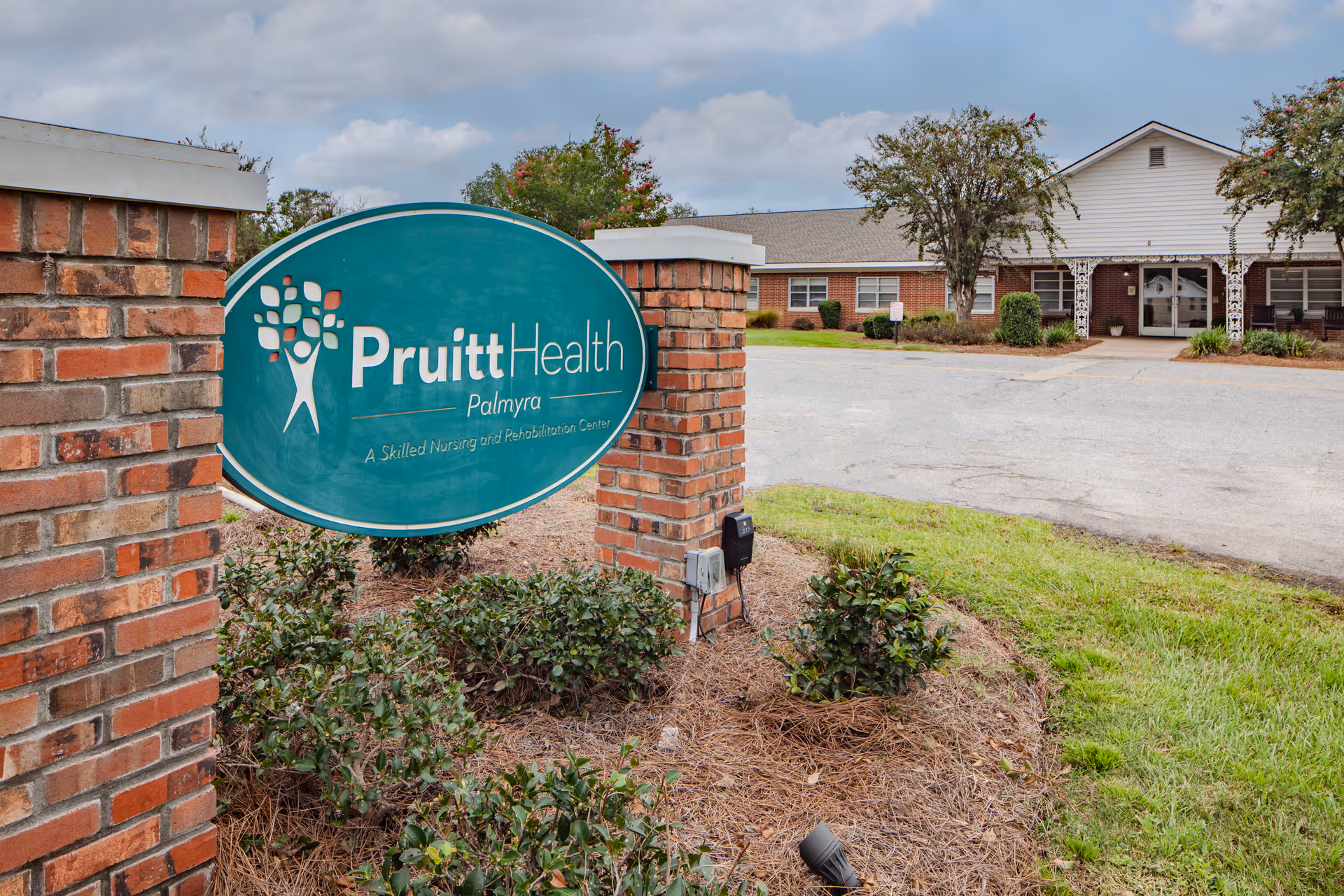 Exterior view of PruittHealth Palmyra facility with a curved teal sign and front entrance.