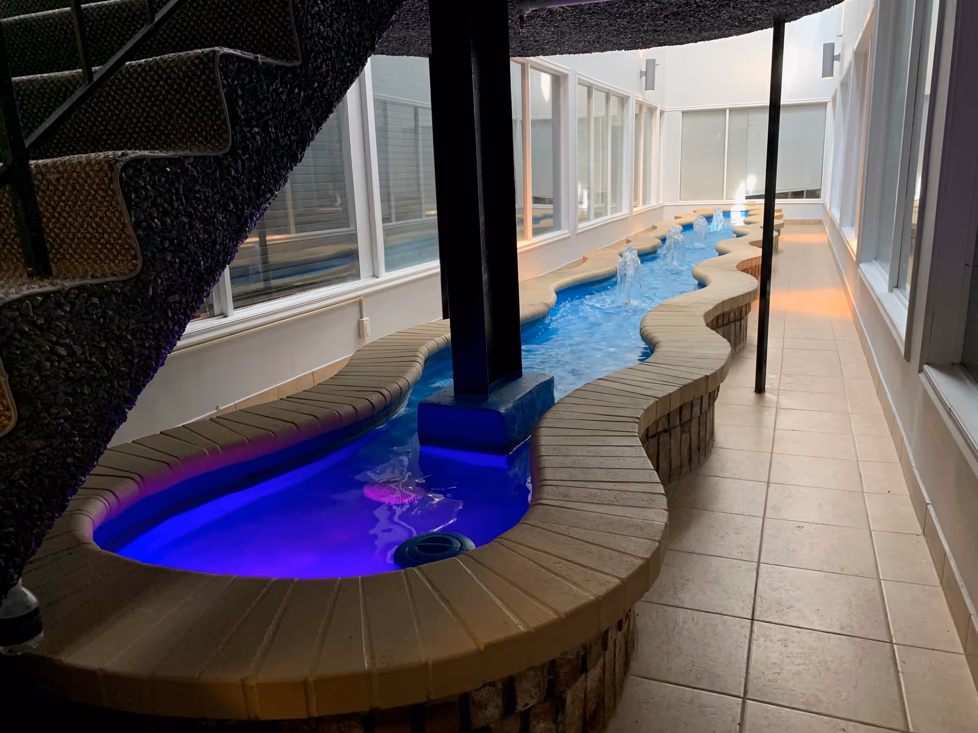 Indoor pool area with curved brick benches and blue-lit water by large windows