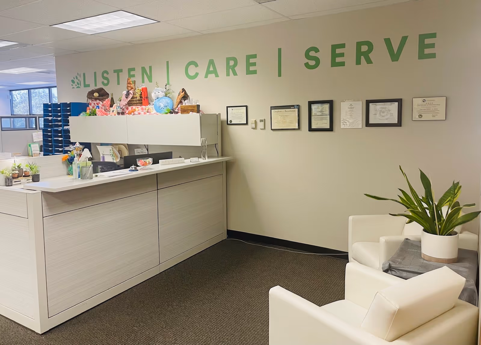 Reception area with a white counter, seating, and wall certificates.