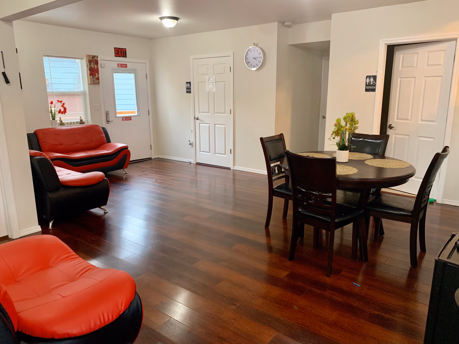 A spacious senior living common area with red and black seating and a round dining table.