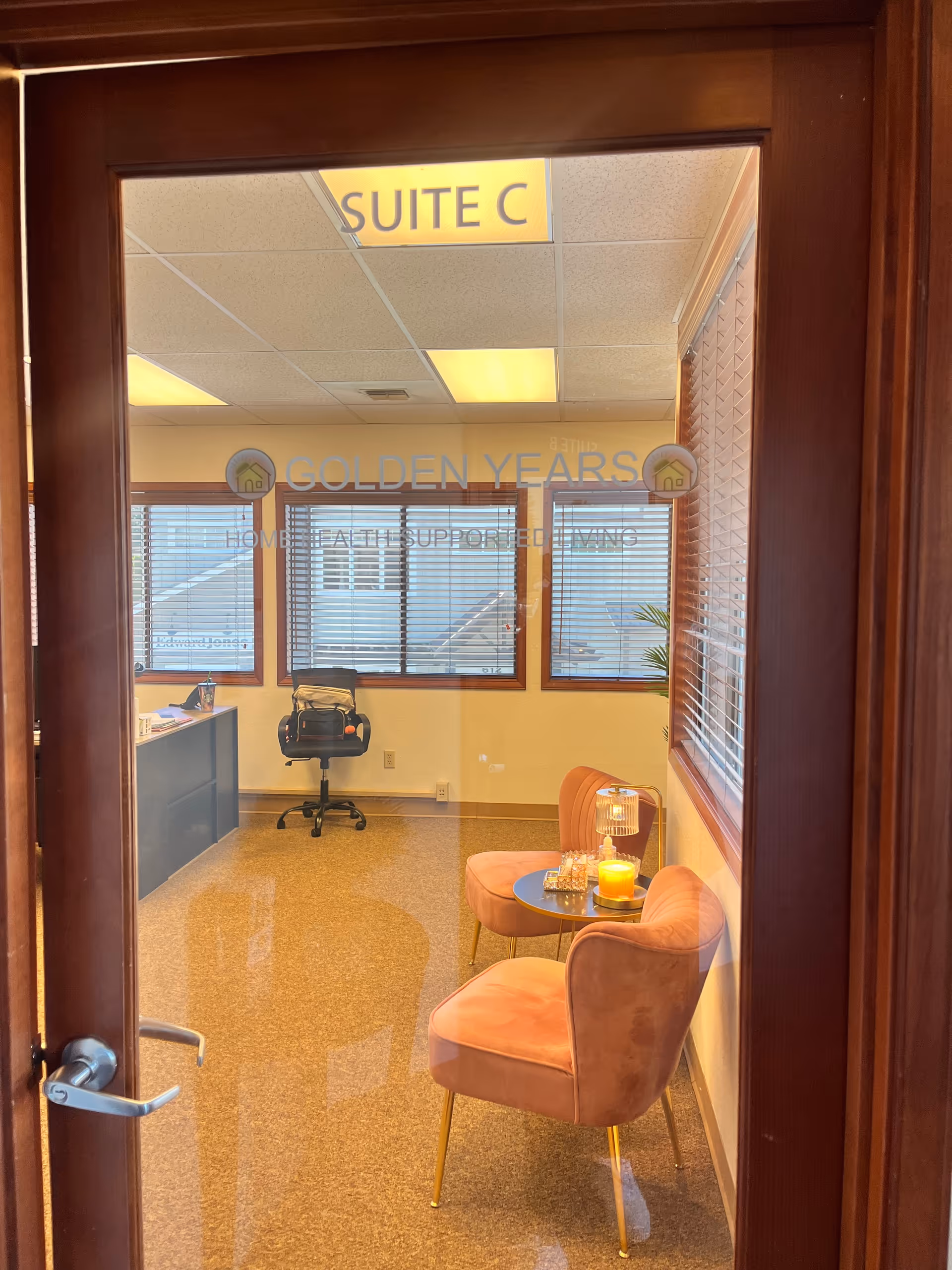 Doorway view into a small office suite with pink chairs and a candlelit table.