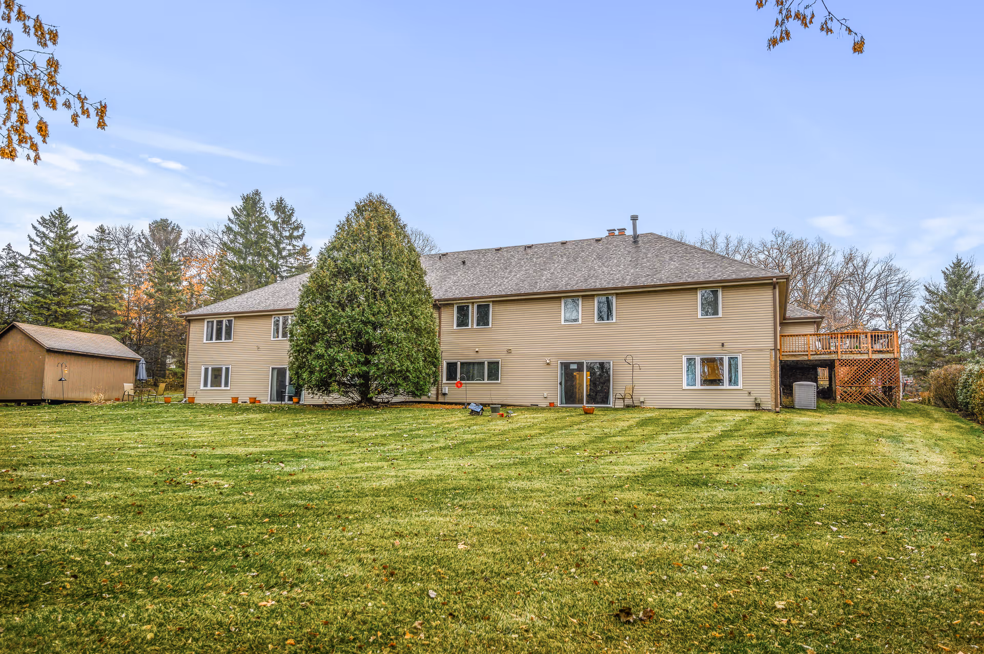 Two-story beige house with a large grassy yard and wooden deck.