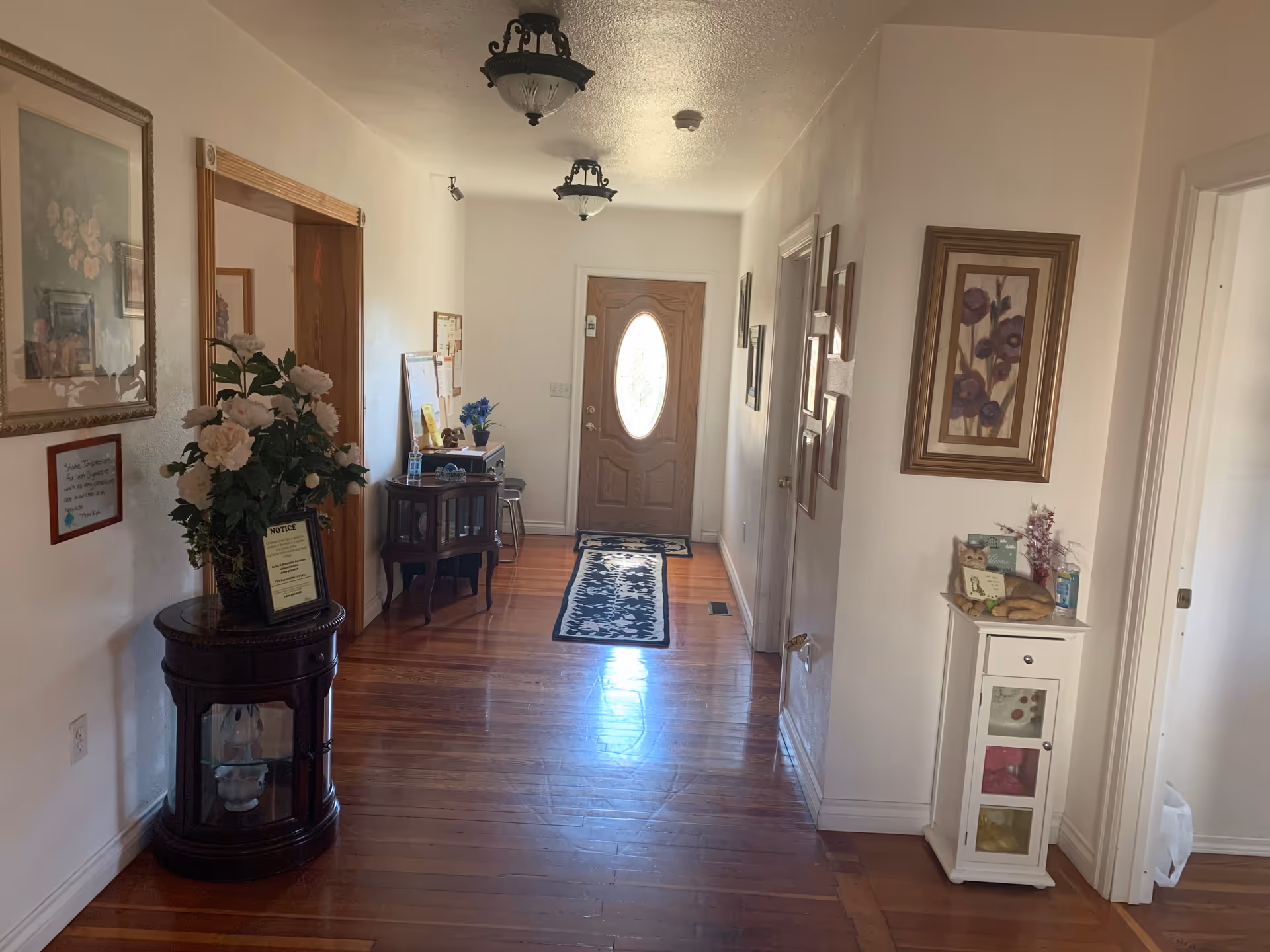 Bright hallway inside a senior living facility with wooden floors, art, and a front door.