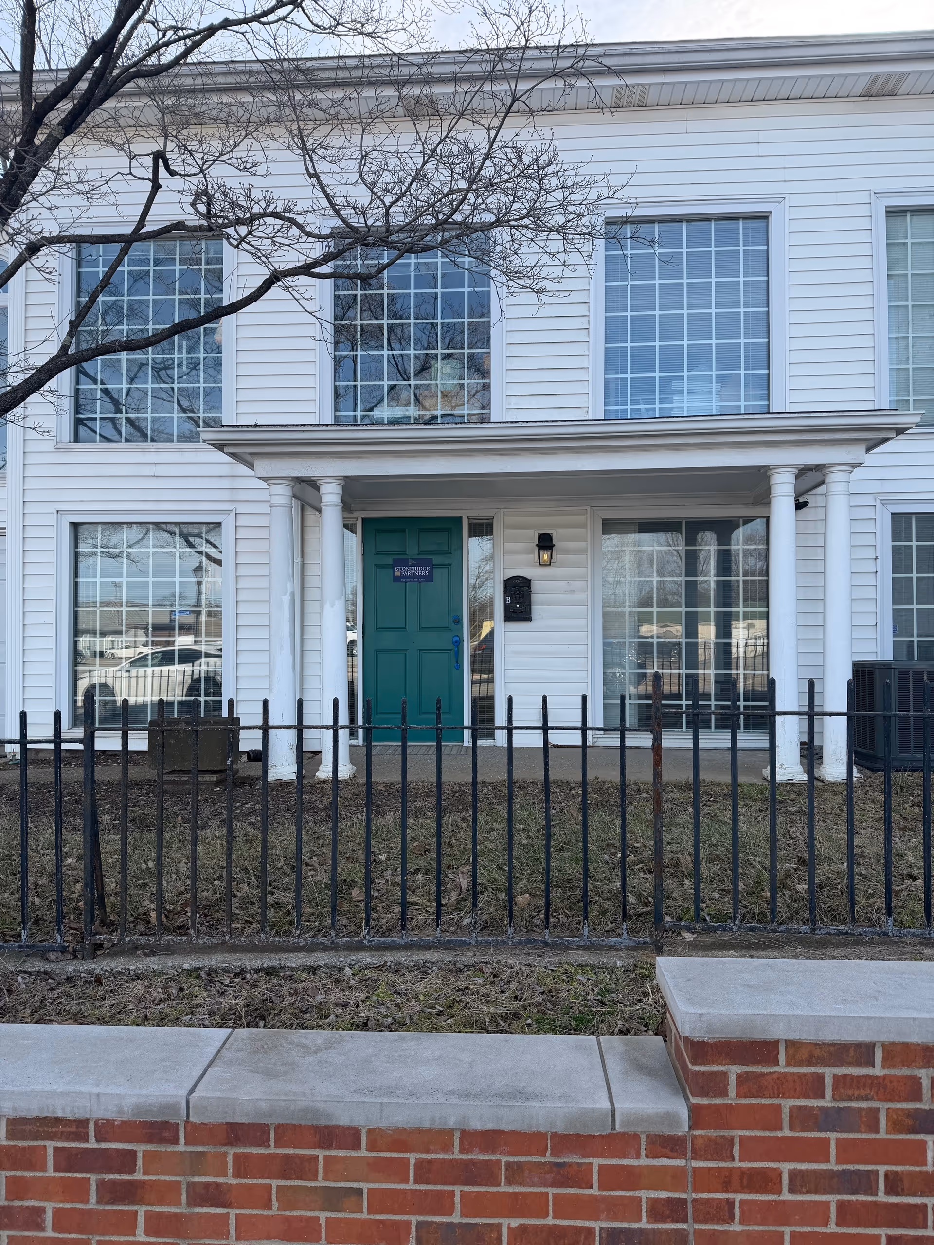 White two-story building with teal front door, columns, and a black metal fence.