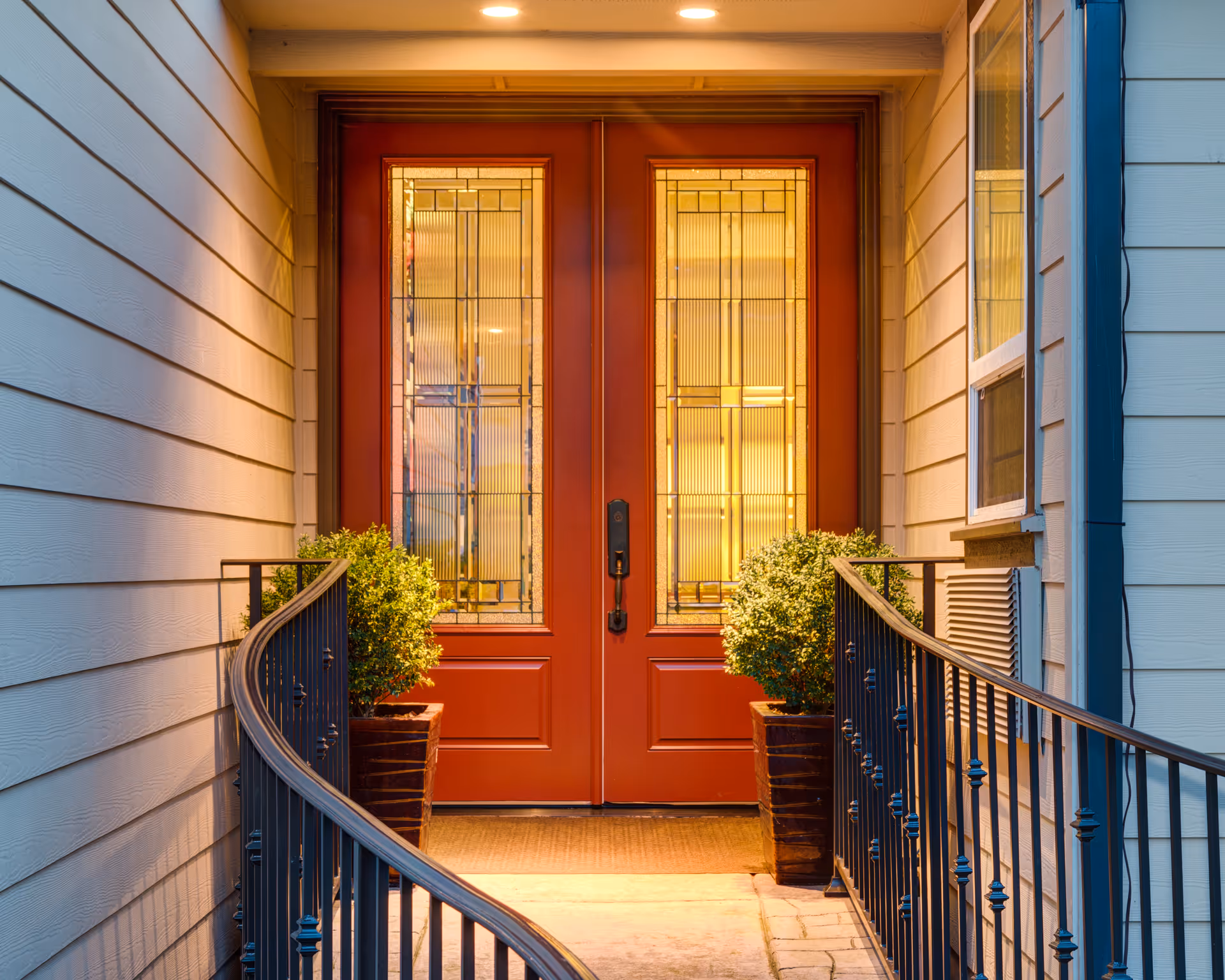 Exterior entrance with red double doors, glass panels, and potted plants beside the entry.