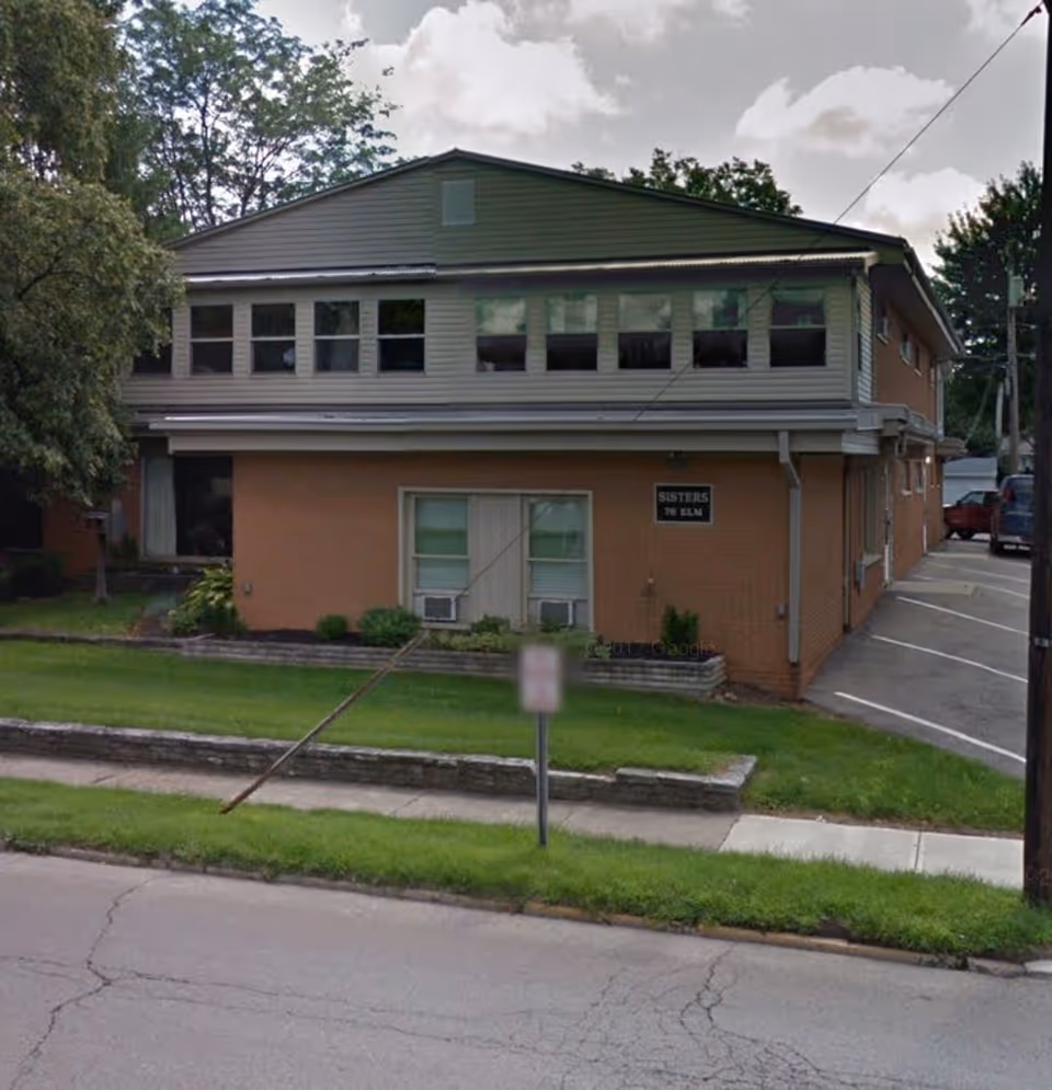 Two-story brick building with large upper windows and a small sign on the front façade.