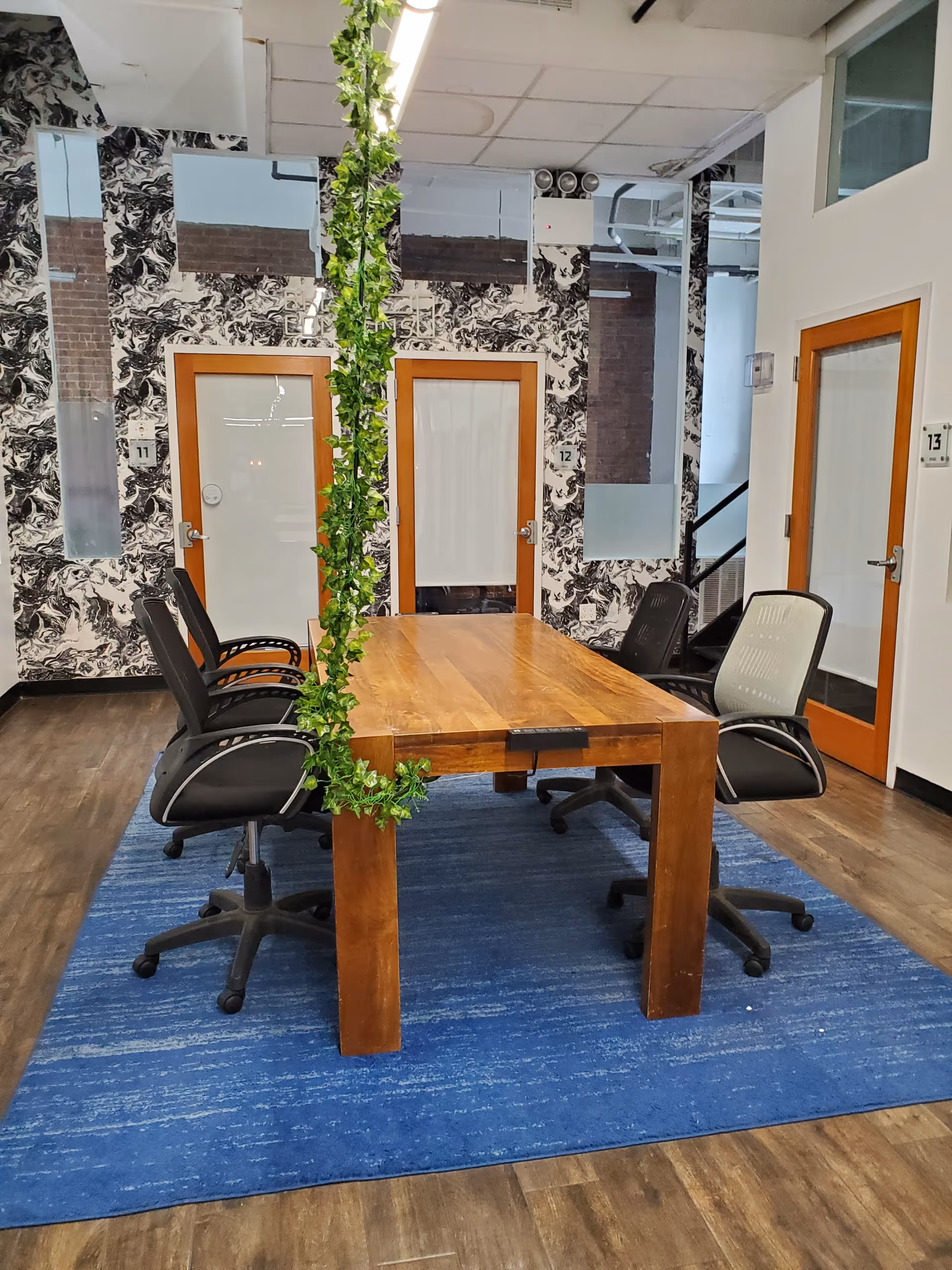 Wooden conference table with chairs around, ivy garland hanging from ceiling in modern interior.