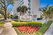 Tall pale building with a landscaped entry and a sign in front of red flower bed.