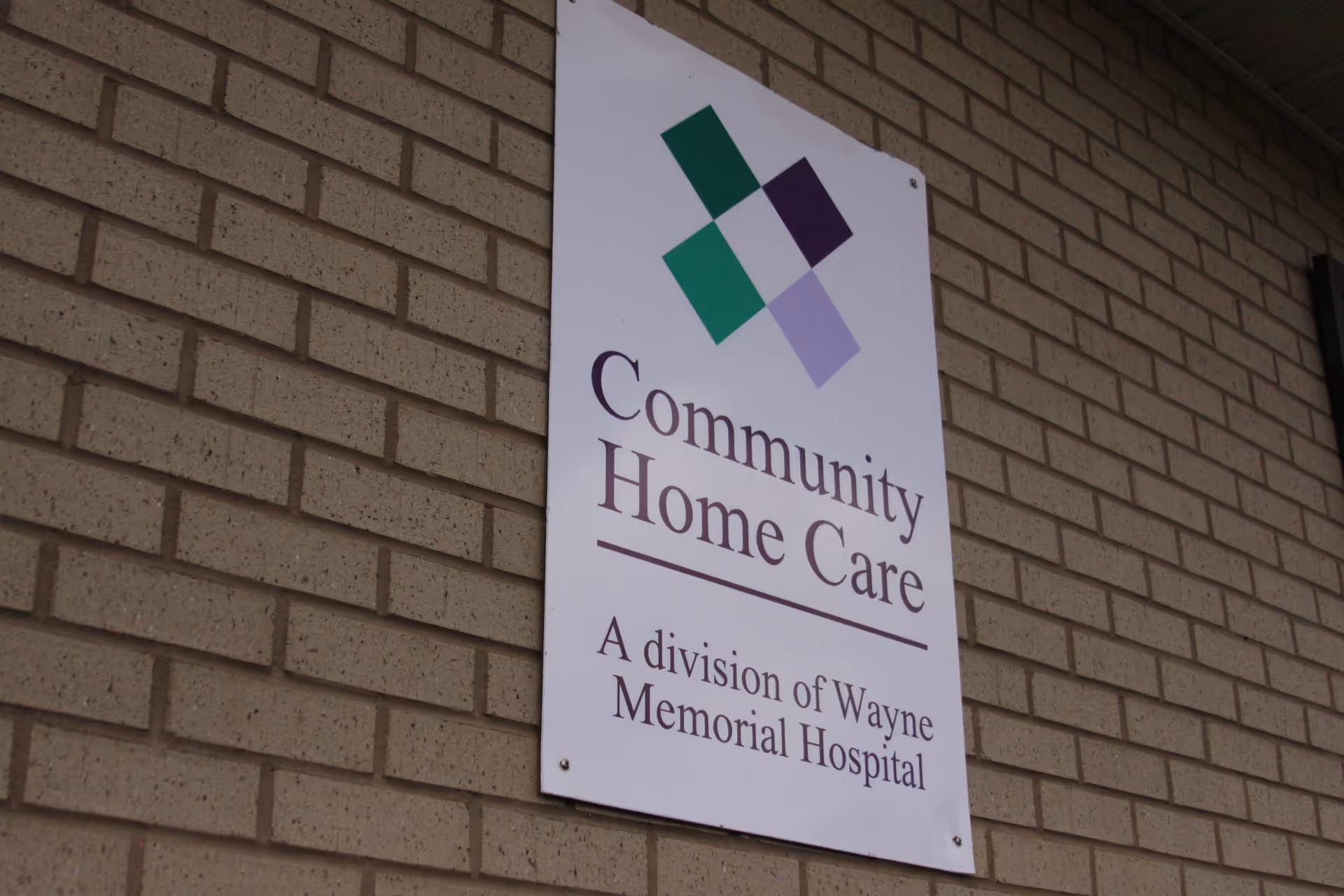 A brick exterior wall sign reads: Community Home Care, a division of Wayne Memorial Hospital.
