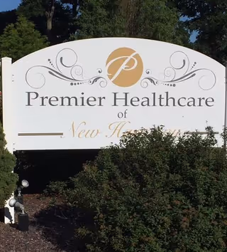 White outdoor sign reading "Premier Healthcare of New Harmony" set among shrubs and trees.