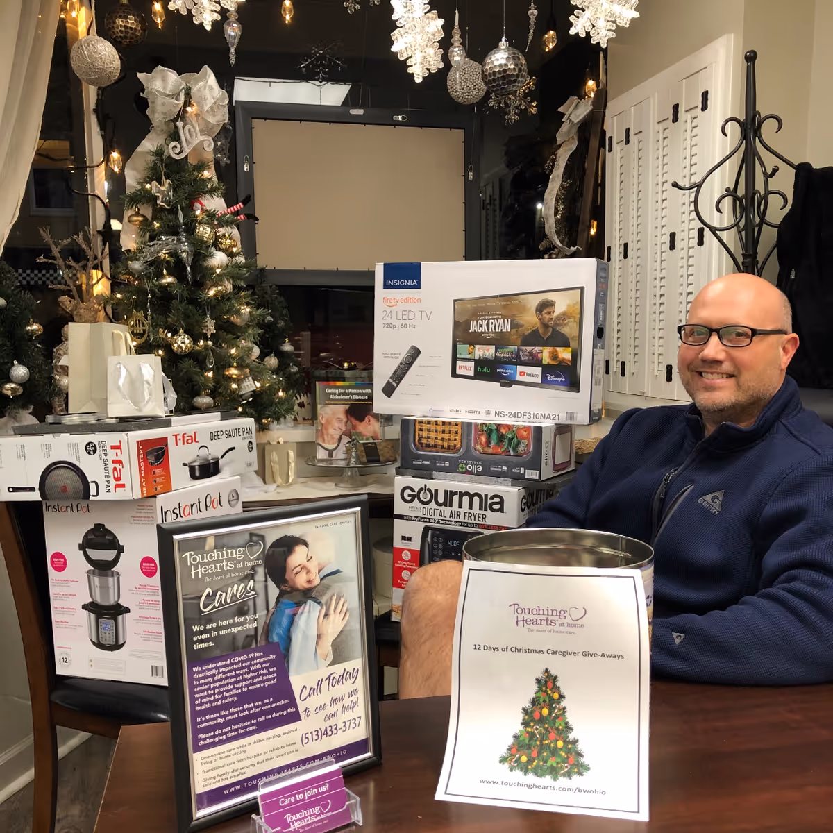 Smiling man sits at a table surrounded by boxed appliances and holiday decor.