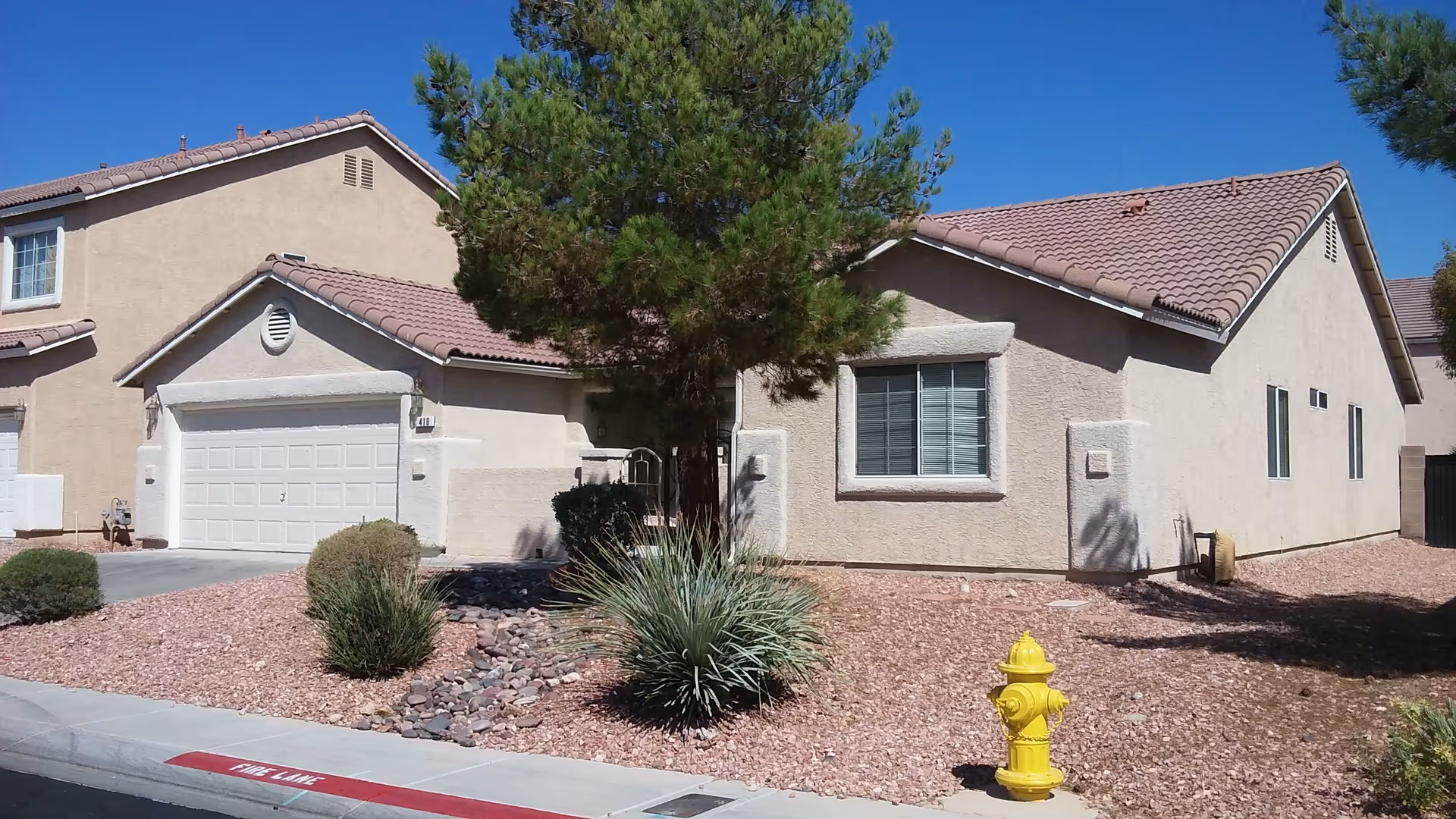 Front exterior view of a beige single-story building with a tree, rocks, and a yellow hydrant.