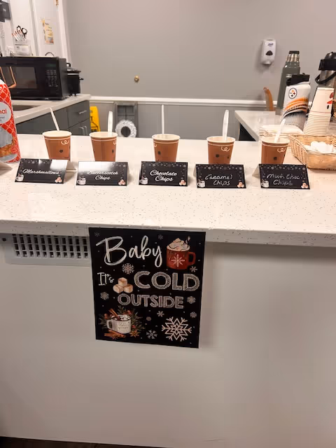 Interior cafe counter with coffee cups, signs, and a 'Baby It's Cold Outside' poster.