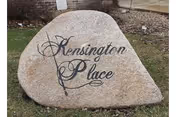A large engraved stone sign on a lawn reading Kensington Place.