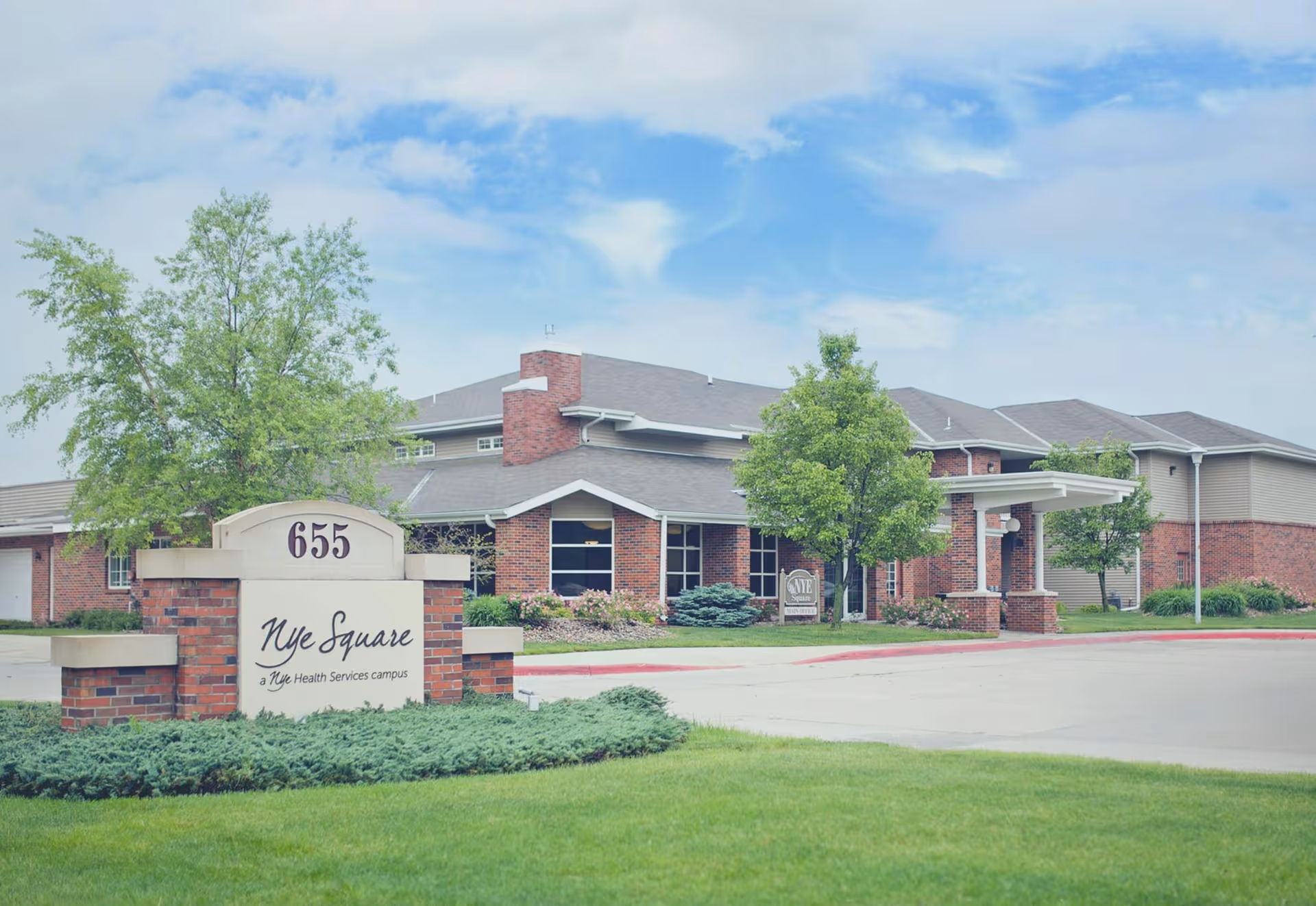 Exterior view of Nye Square senior living facility with brick building and manicured lawn.