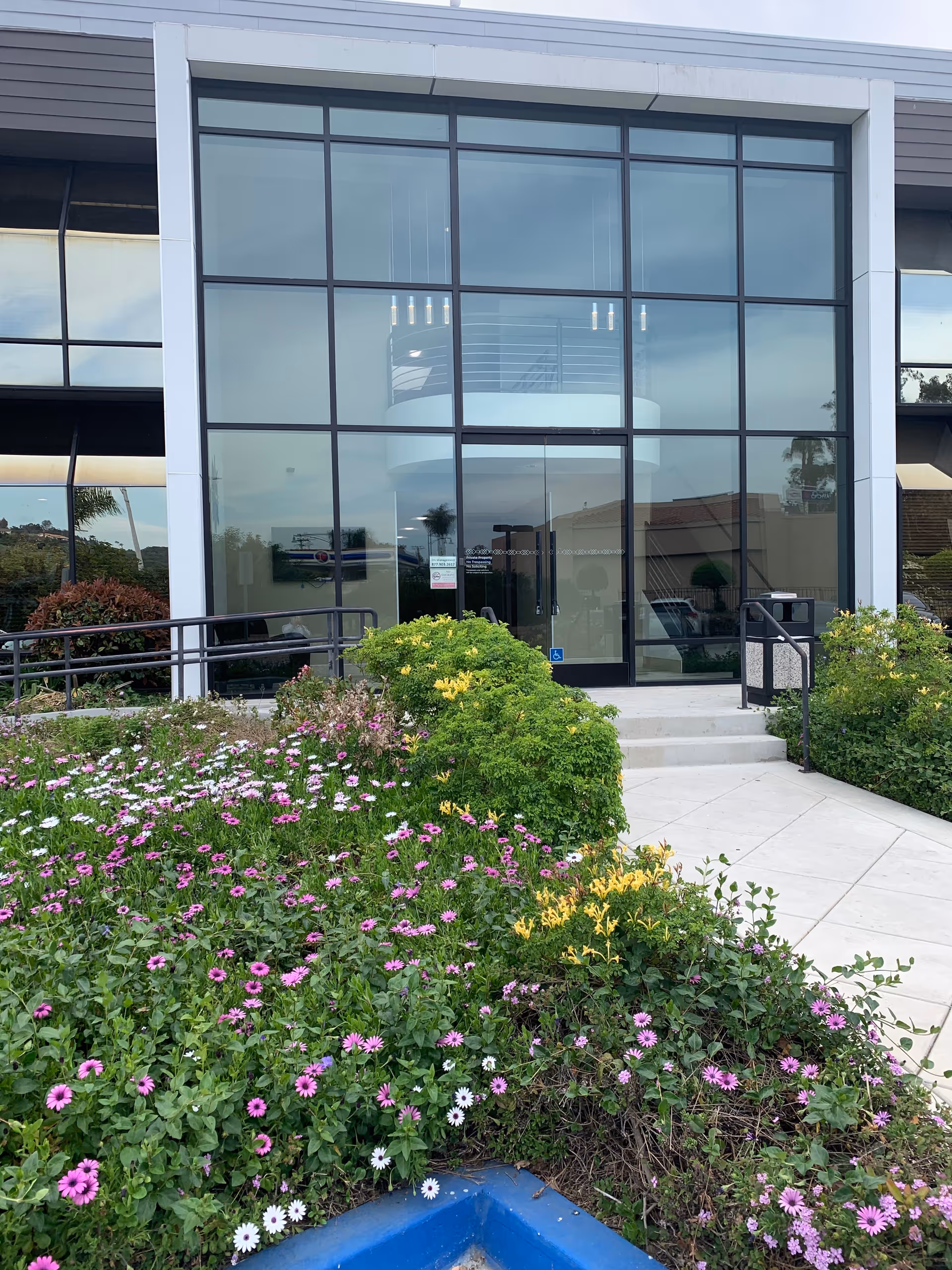 Glass-front entrance of Advent Healthcare Services, Inc. building with landscaped flower beds.
