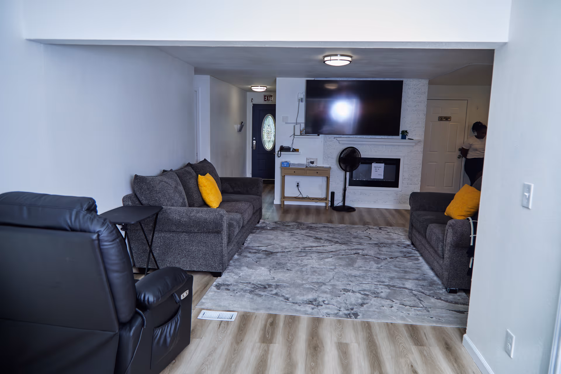 Cozy living room in a senior facility with gray couches, rug, fireplace, and TV.