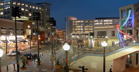 Nighttime exterior view of a modern plaza with buildings, stairs, and a neon sculpture.