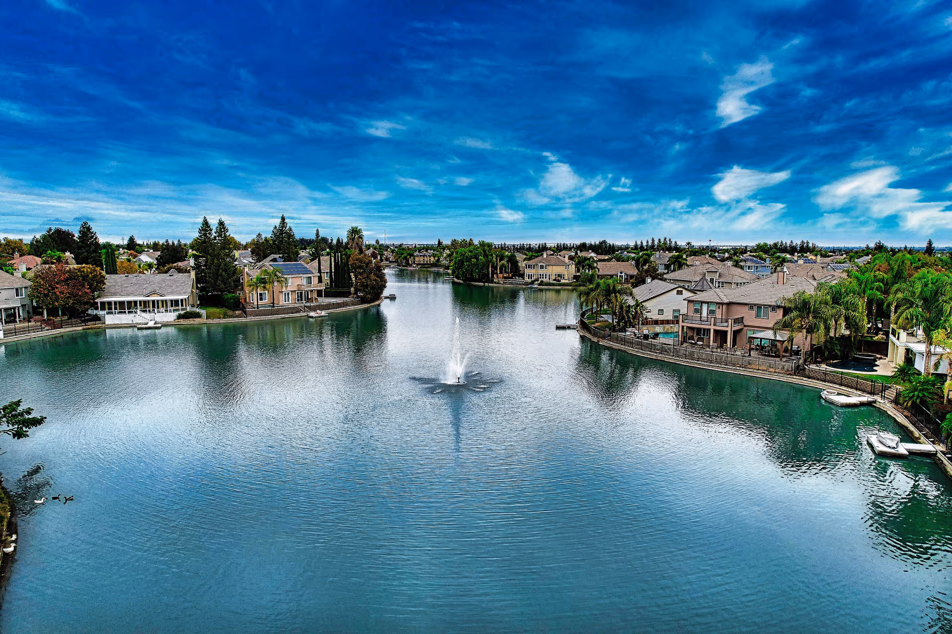 Aerial view of a residential lakefront community with a central fountain and houses.