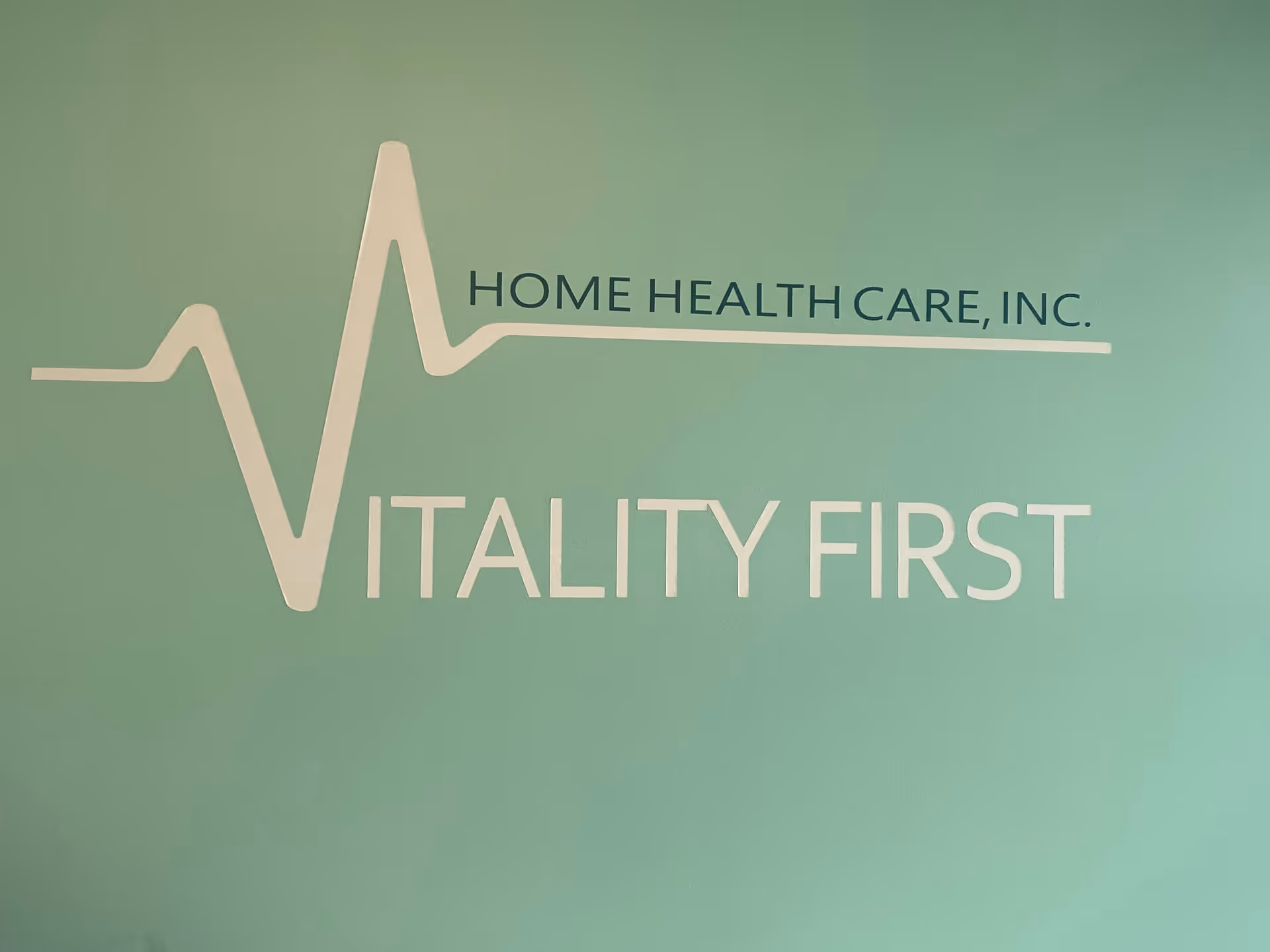 Teal interior wall displaying the Vitality First logo and Home Health Care, Inc. text.