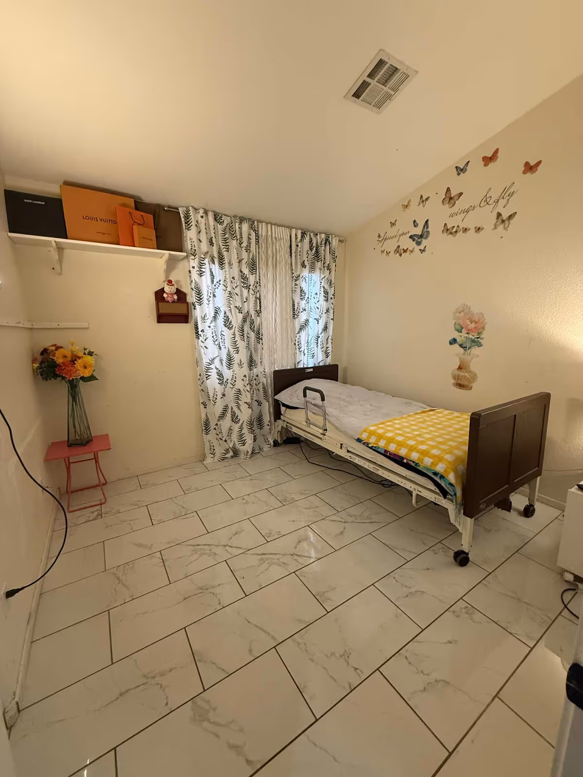 Hospital-style adjustable bed in a decorated bedroom with butterfly decals and floral curtains.