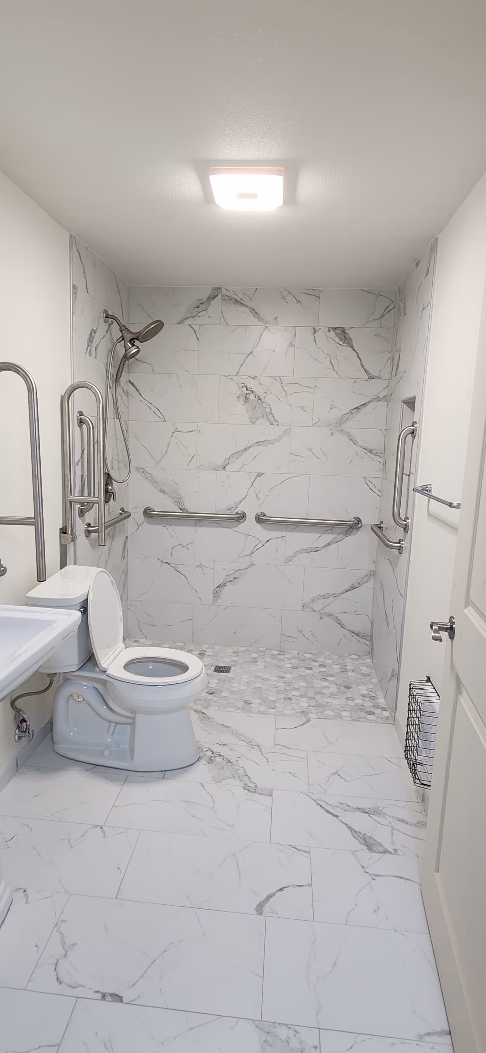 Accessible bathroom with marble tiles, multiple grab bars, toilet, and sink.