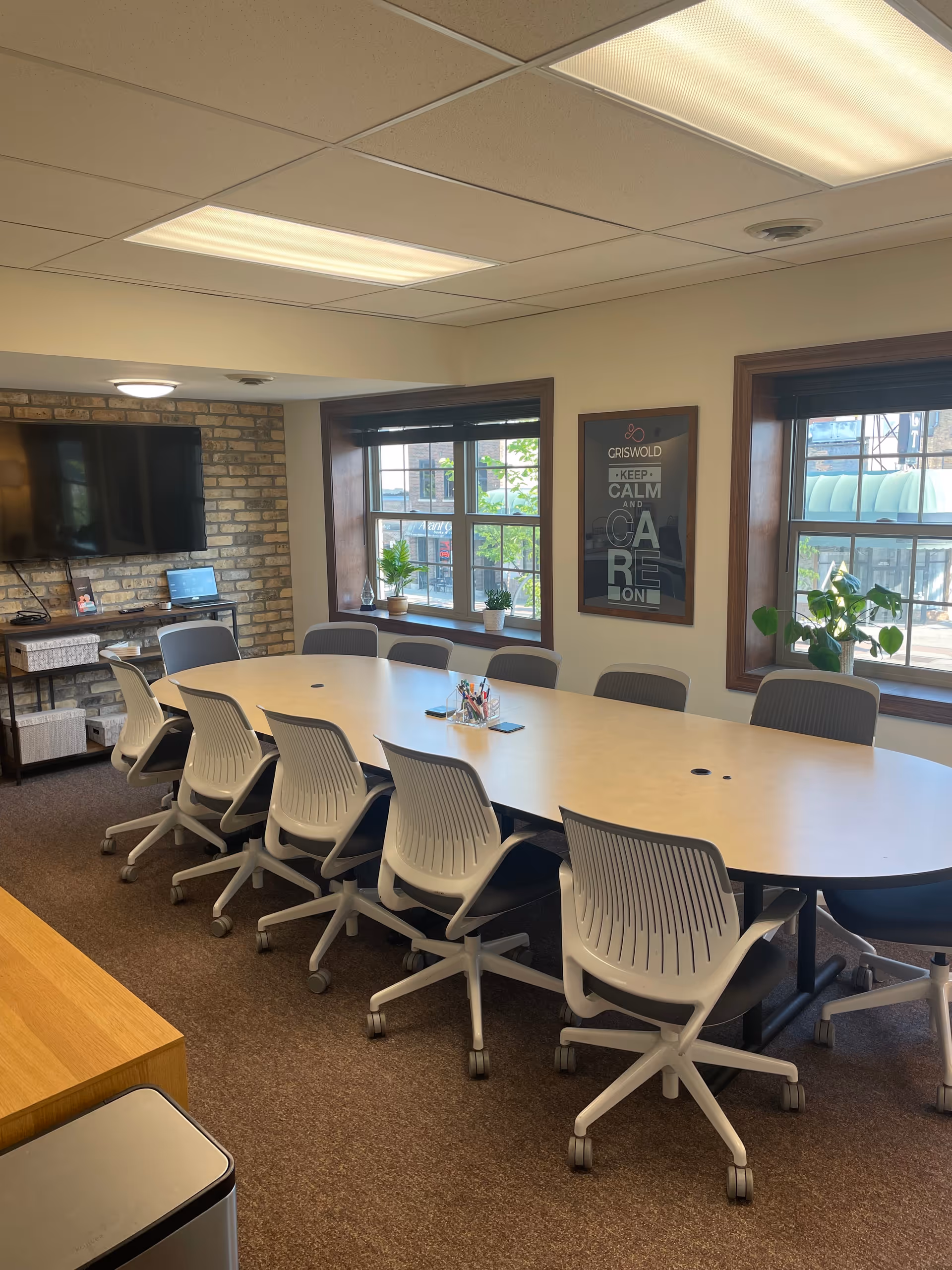 Long conference table with white rolling chairs in a bright, windowed dining room.