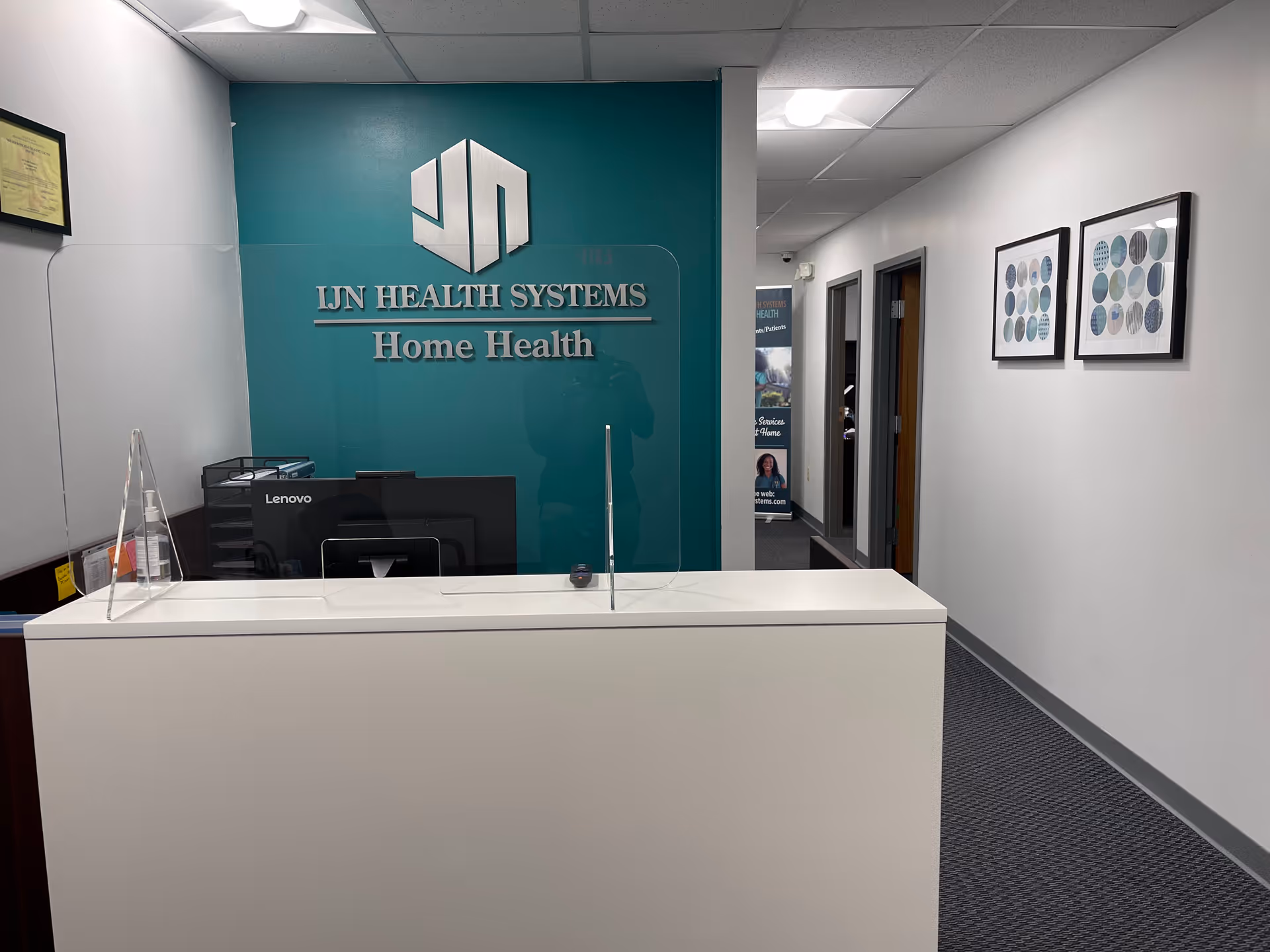 Reception desk in a teal-walled hallway with the IJN Health Systems Home Health logo