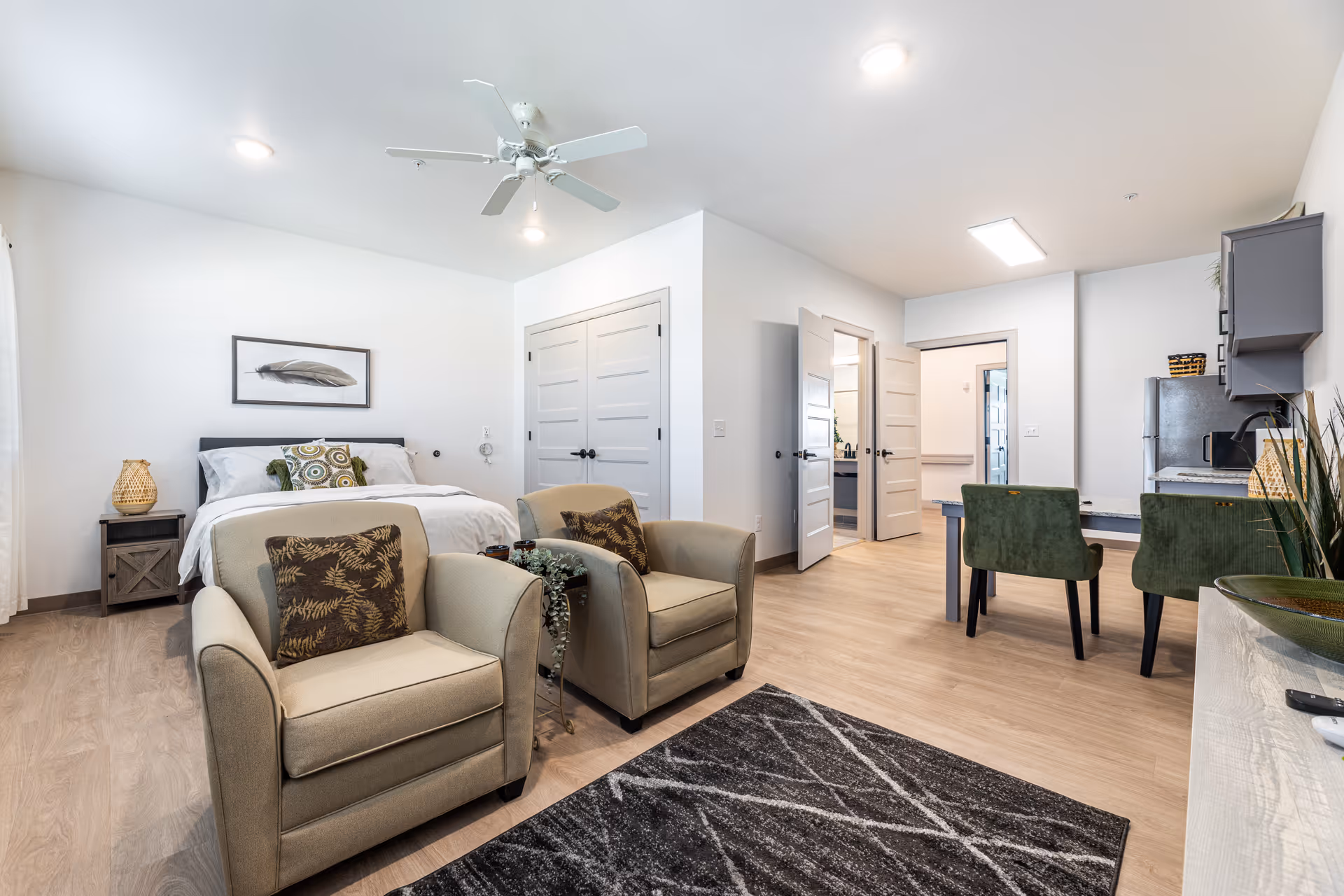 A modern senior living suite featuring a bed, seating area, and kitchenette.