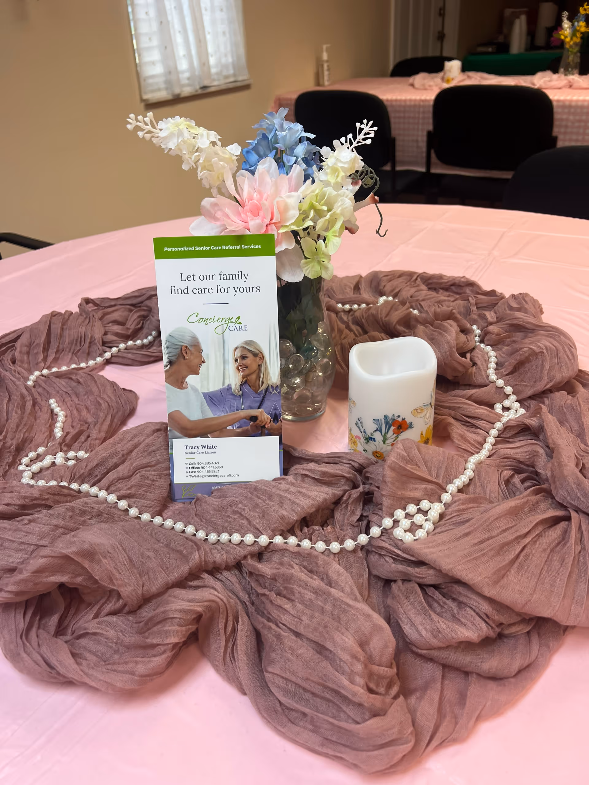 Table centerpiece with pink draped fabric, floral vase, pearls, and Concierge Care brochure.