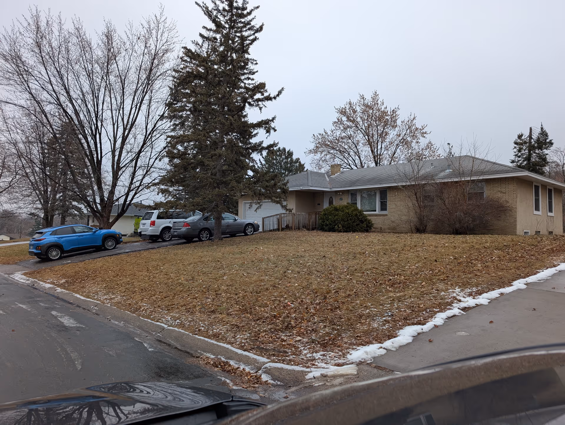 Single-story ranch-style brick home and front yard with a driveway containing several parked cars and bare trees.