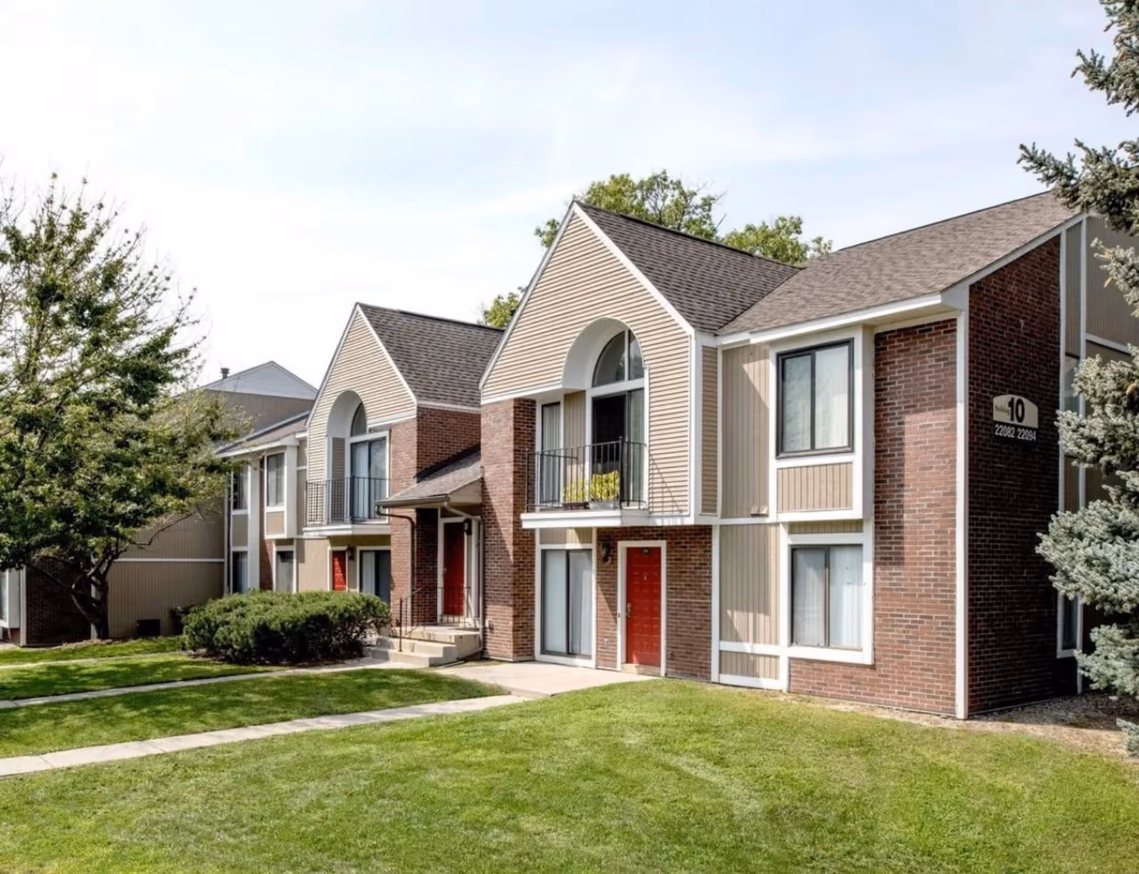 Exterior view of a senior living building with brick walls, red doors, and green lawn.