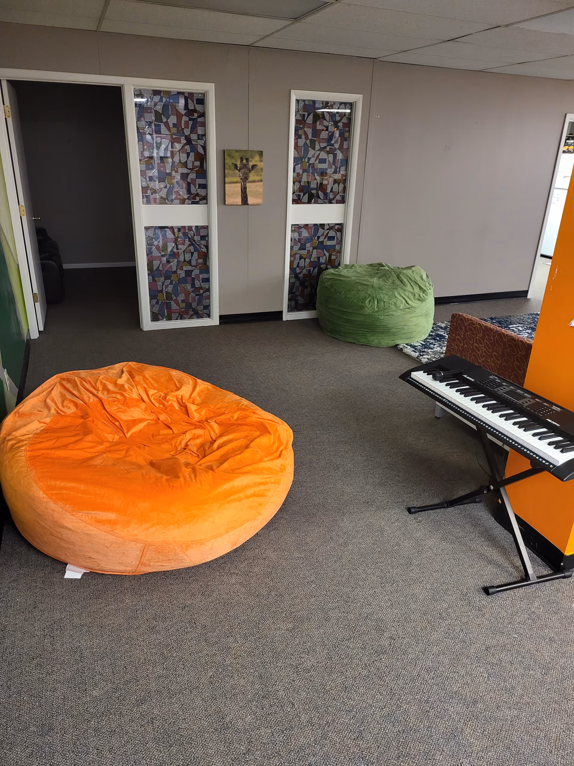 Colorful bean bags, a keyboard on a stand, and a patterned wall in an indoor lounge.