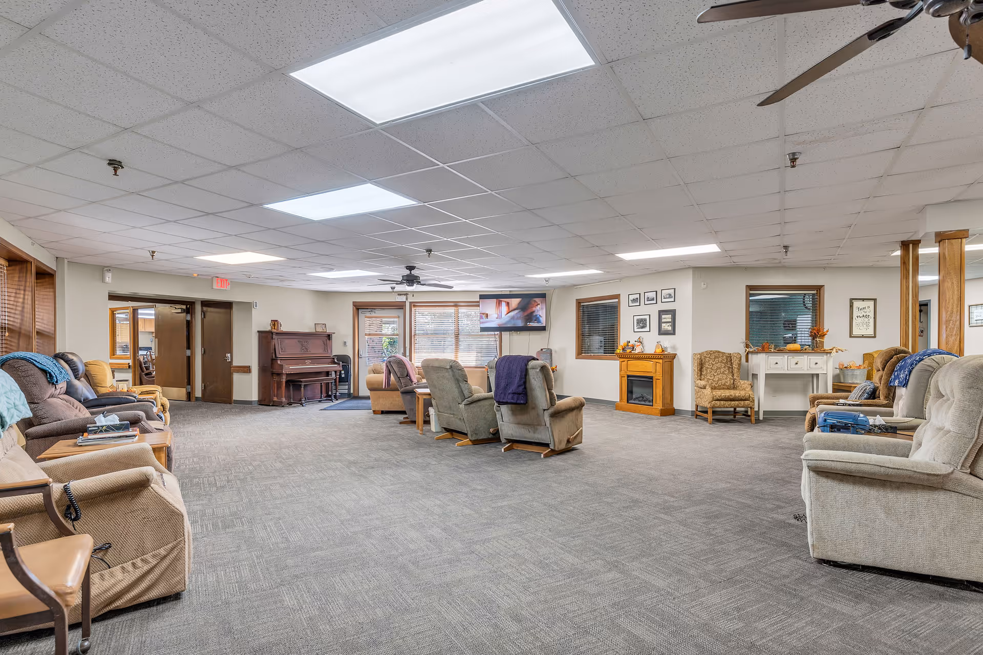 Spacious senior living facility lounge with recliners, sofa seating, piano, and fireplace.