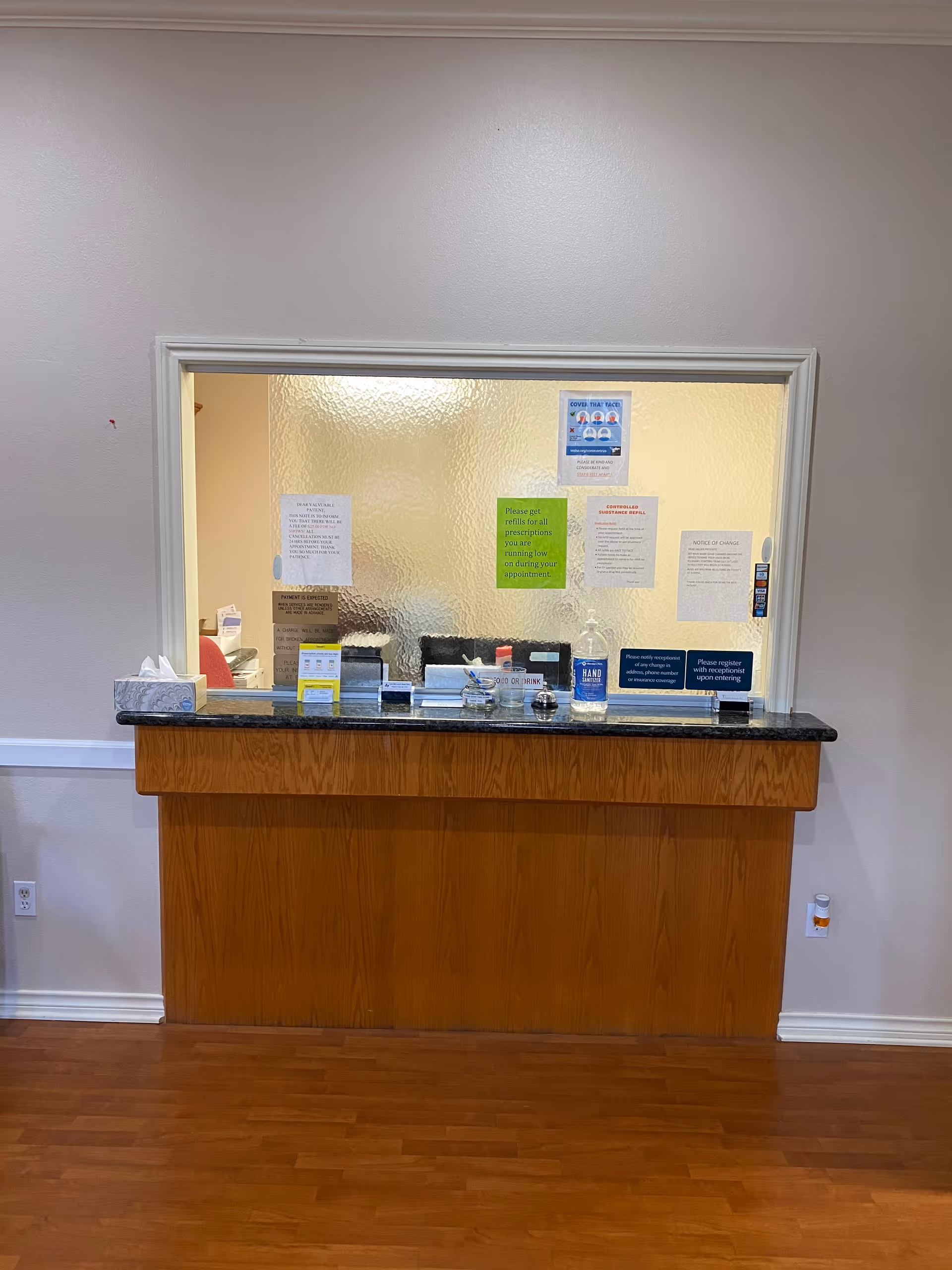 Wooden reception counter with papers behind frosted glass in a clinic interior.