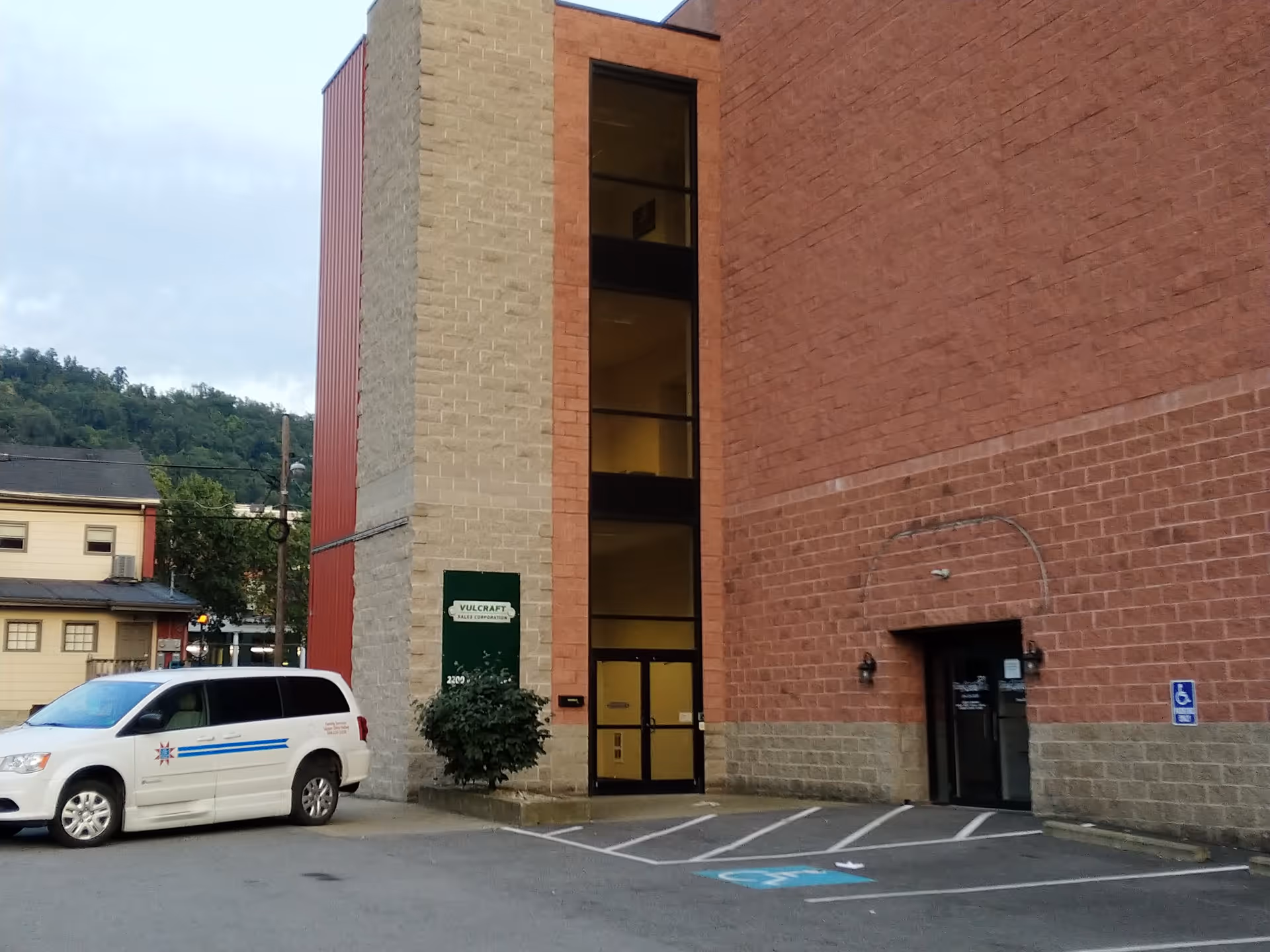 Exterior view of a brick building with a glass entrance and a parked white van.