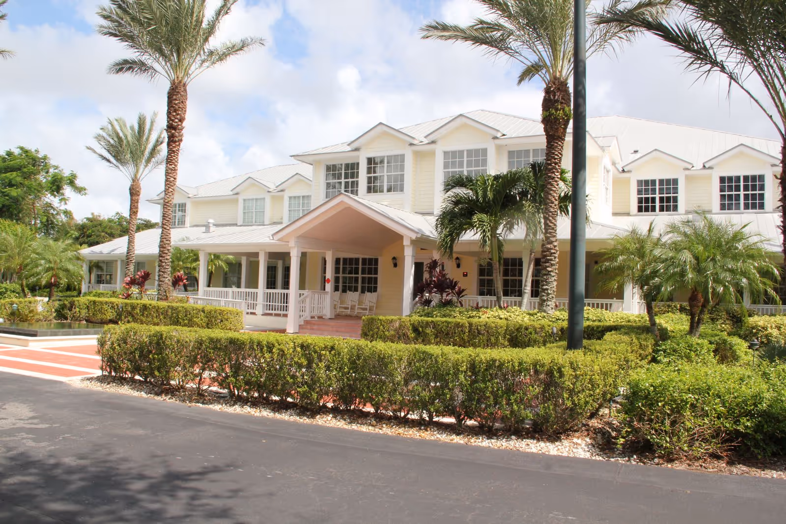 Exterior view of Treasure Coast Hospice building with a covered entrance, palm trees, and trimmed hedges.