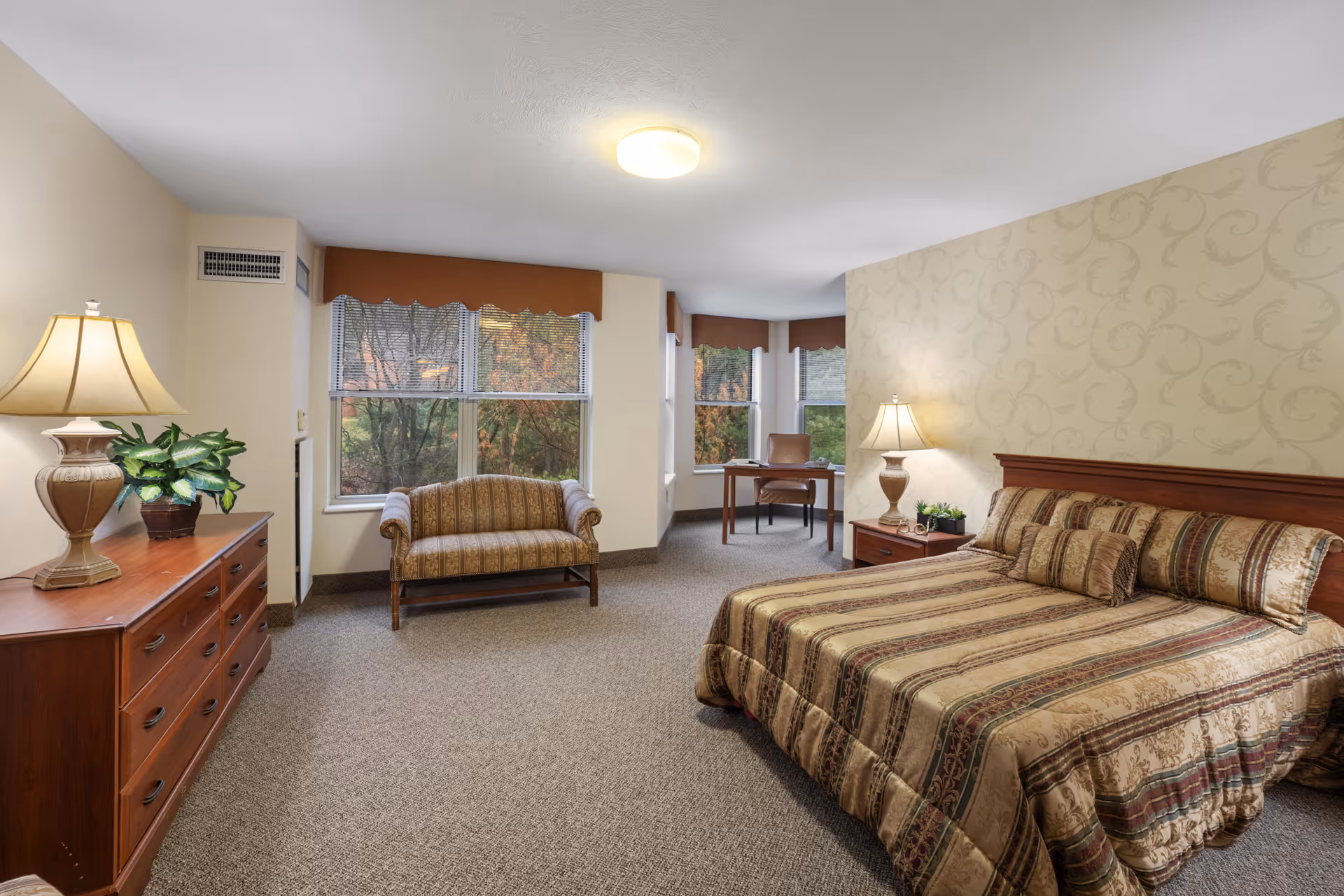 Well-appointed bedroom suite with bed, dresser, seating area, and large windows.