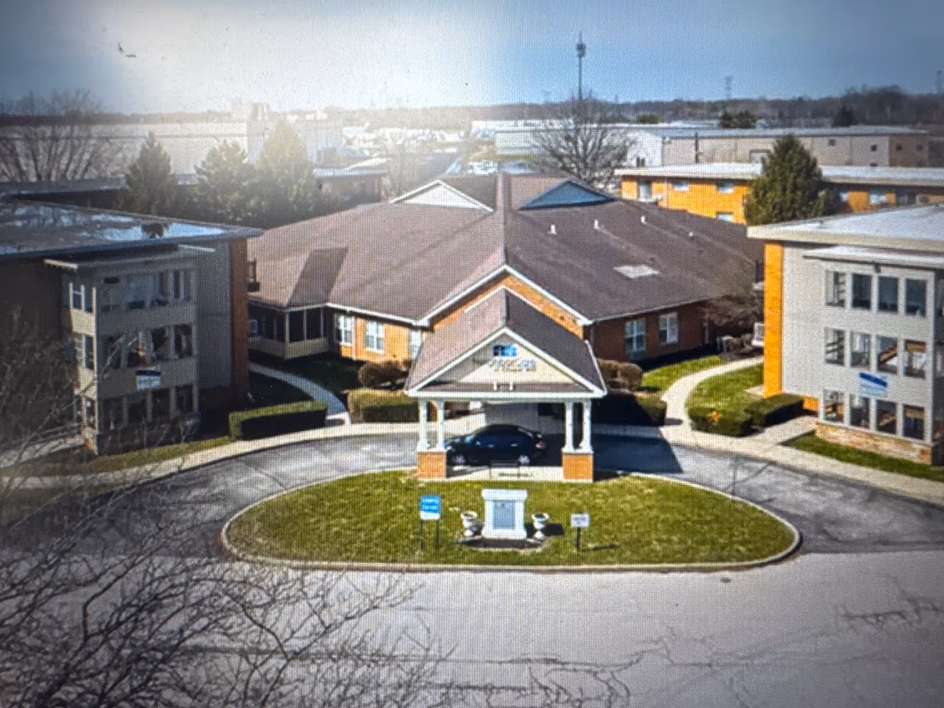 Aerial view of Pinnacle West Apartments entrance with circular driveway and surrounding buildings.