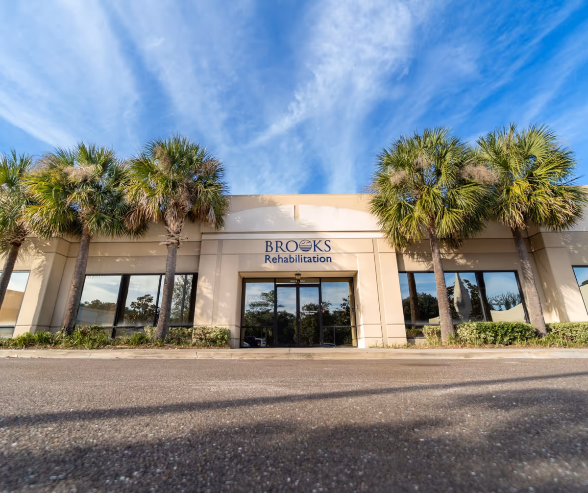 Front exterior of Brooks Rehabilitation Home Health Corporate Center with palm trees and glass entrance.