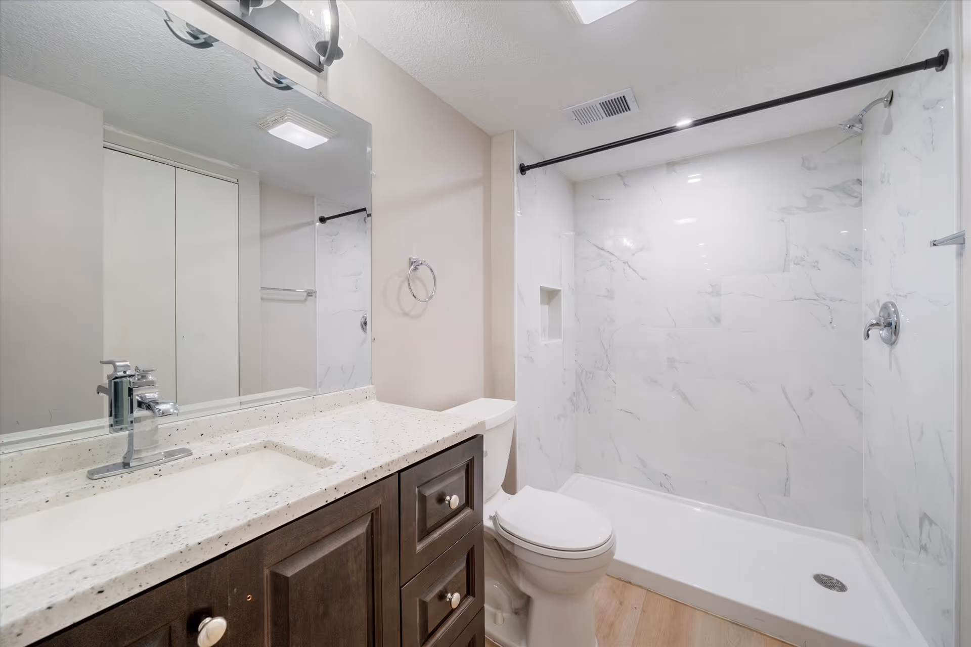 Modern bathroom with double-sink vanity, toilet, and marble-tiled shower.