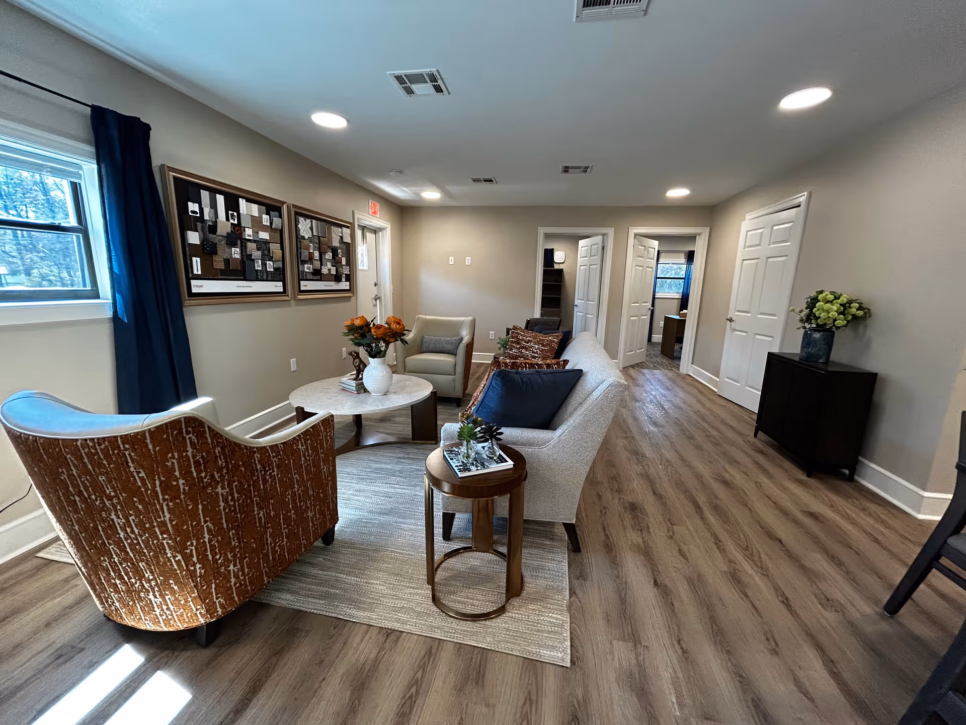 Well-lit senior living lounge with sofa, chairs, coffee tables, wall art, and a window.